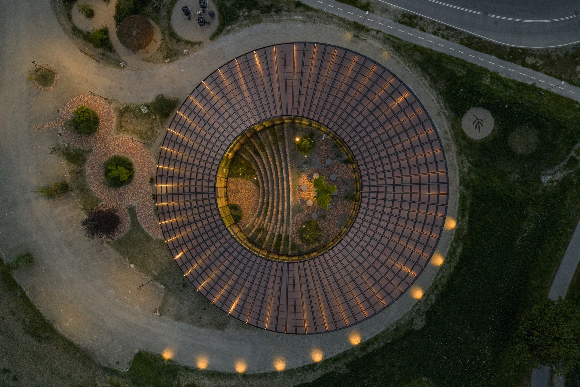 Aerial view of circular brick amphitheater with concentric rings of paving illuminated at twilight
