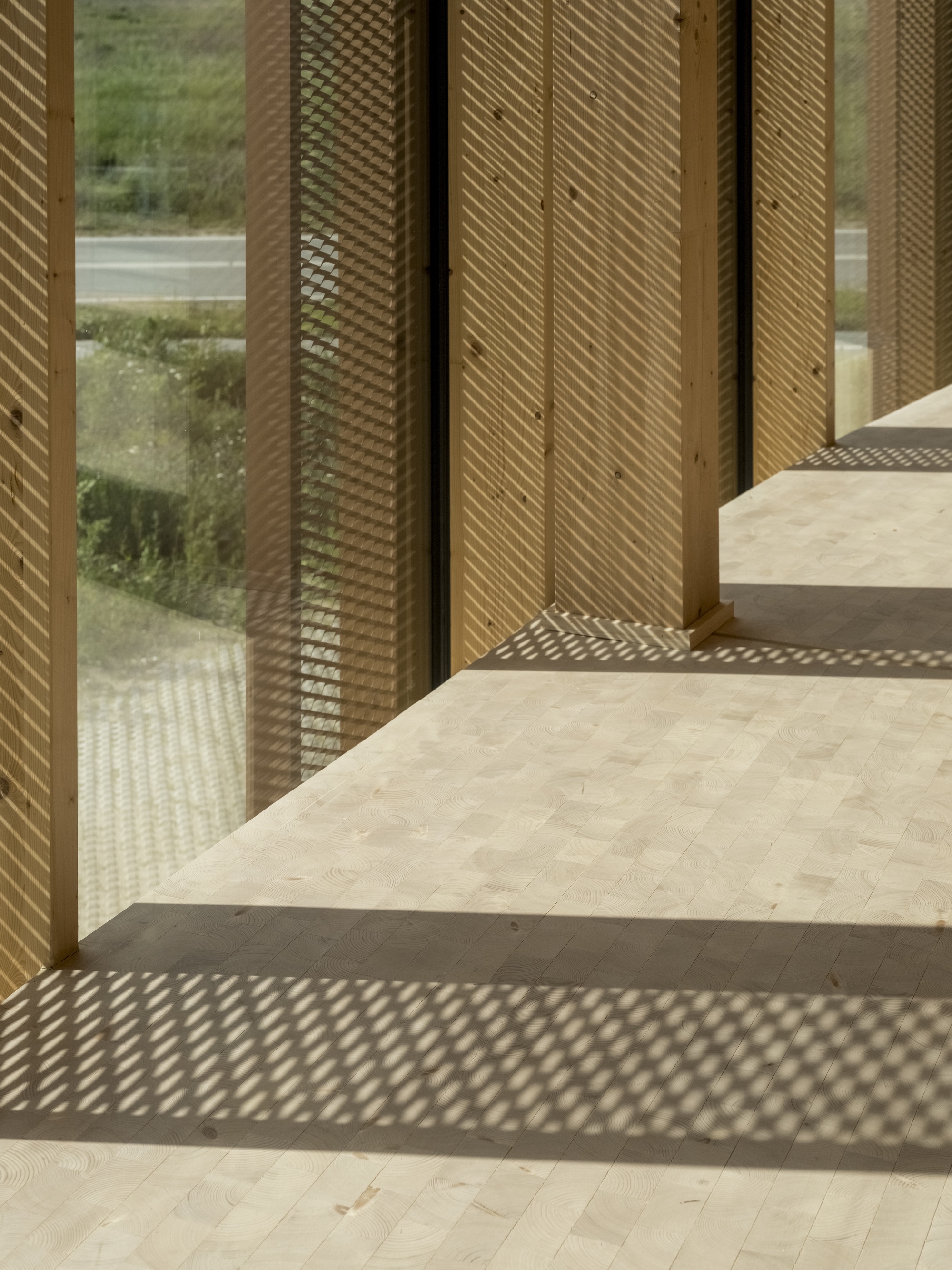 Perforated metal screens beside timber columns creating dappled light patterns on pale flooring