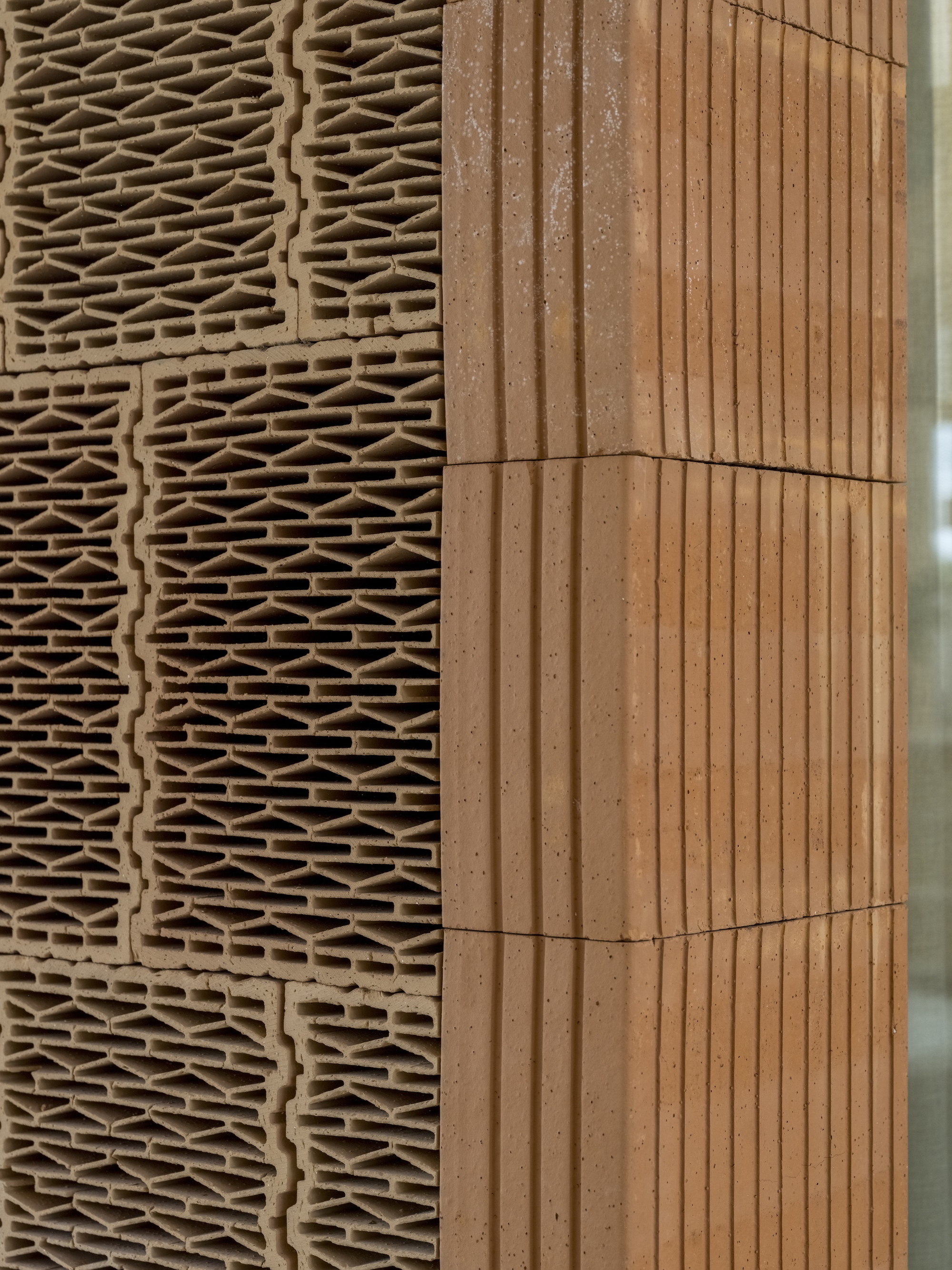 Detail junction of ridged terracotta panel meeting corrugated timber cladding at an angle