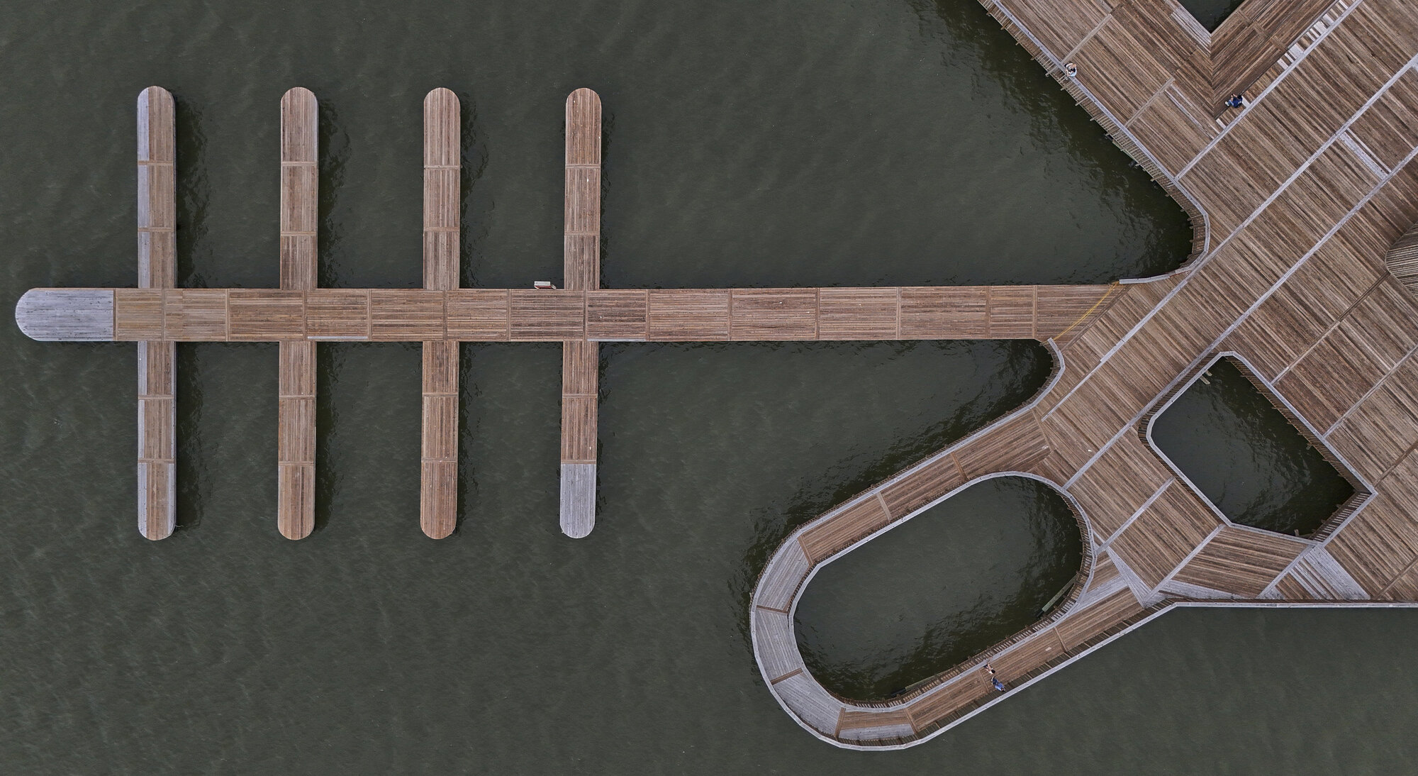 Overhead view of timber pier with rounded and angular platforms extending over dark water