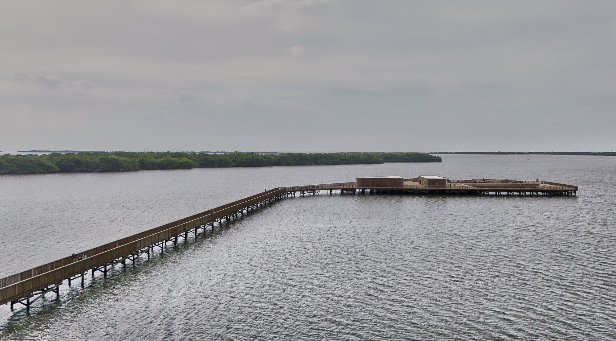 Elevated timber boardwalk extending across open water toward distant viewing pavilion under overcast sky