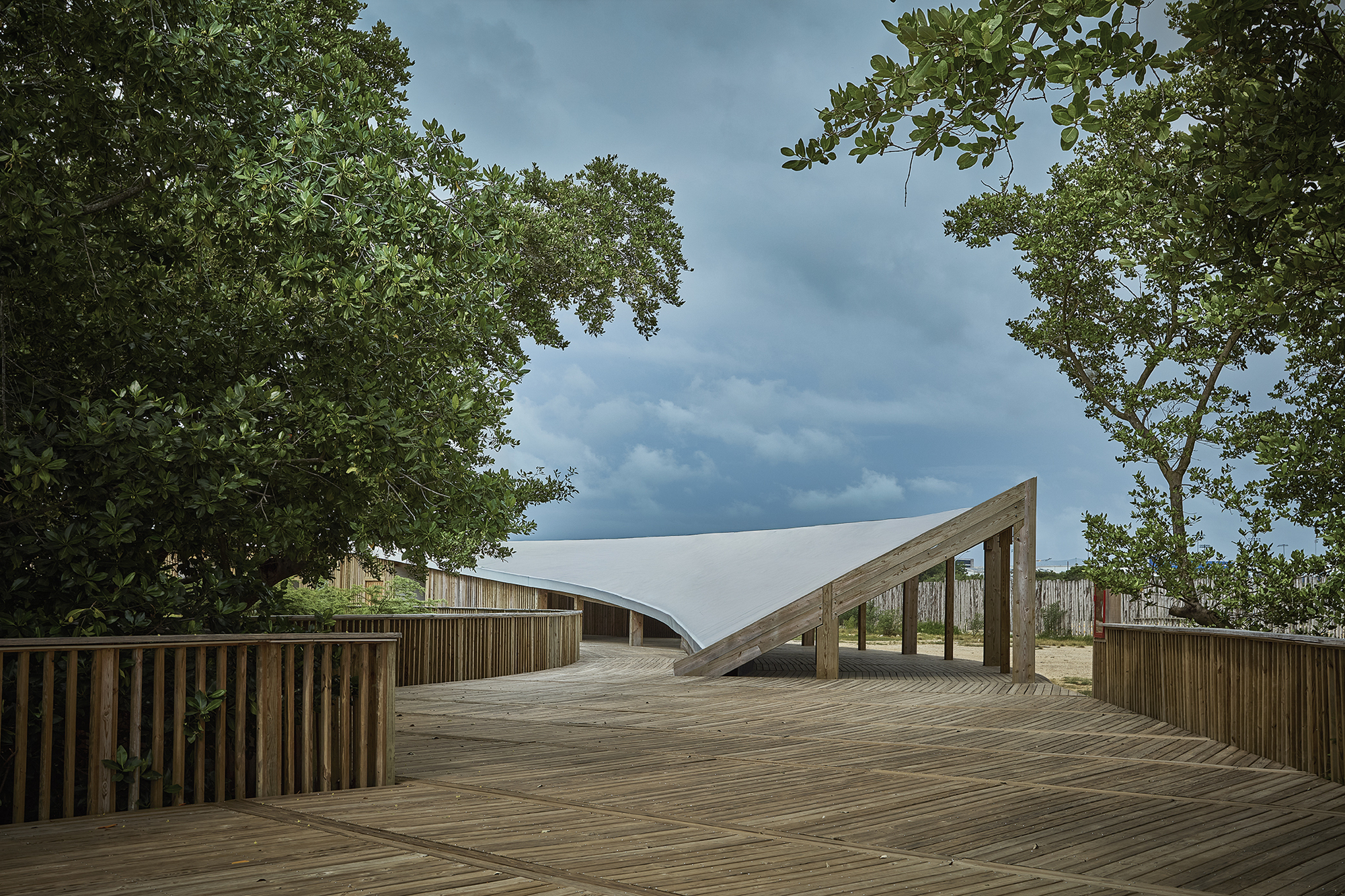 Timber deck with angled structural gateway framing white tensile canopy between mature trees