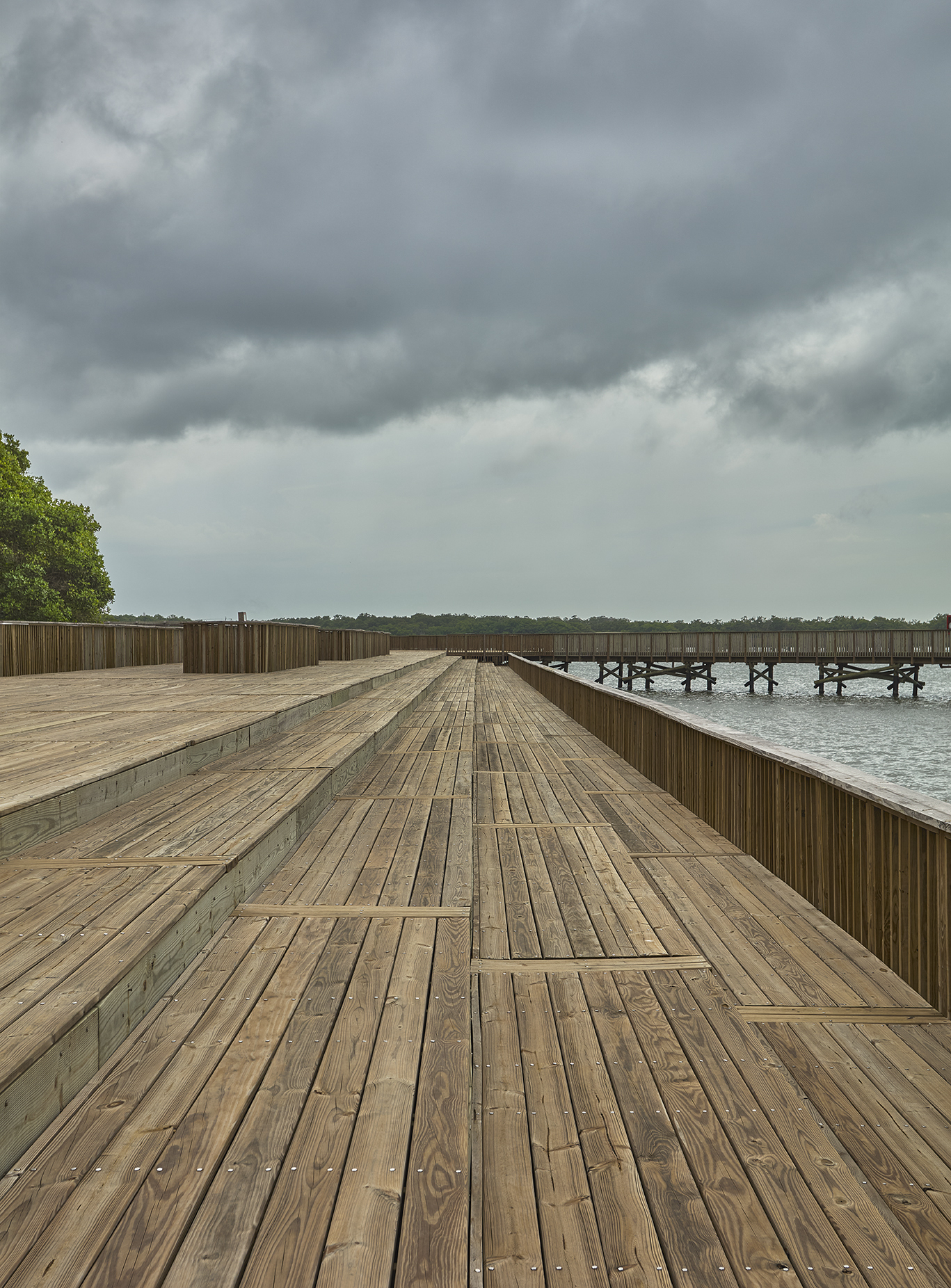 Timber deck with alternating board pattern flanked by vertical slat railings under heavy cloud cover