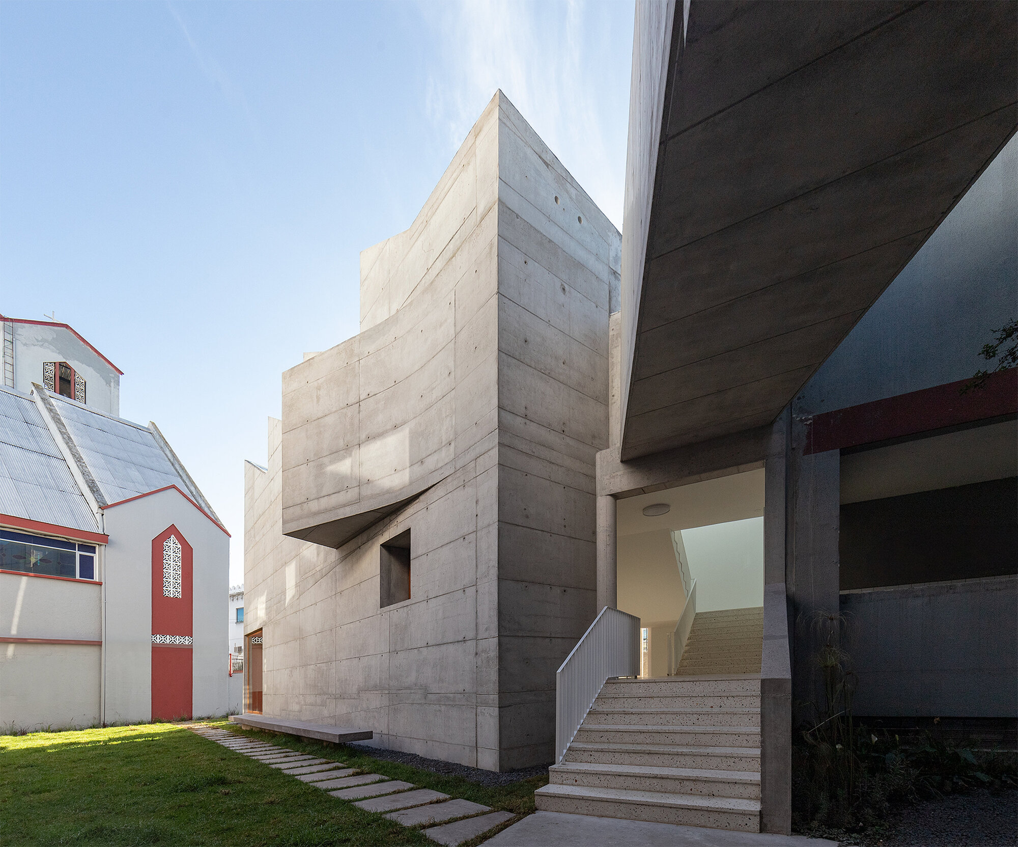 Exterior concrete staircase leading to an entrance beneath a cantilevered volume on a clear day