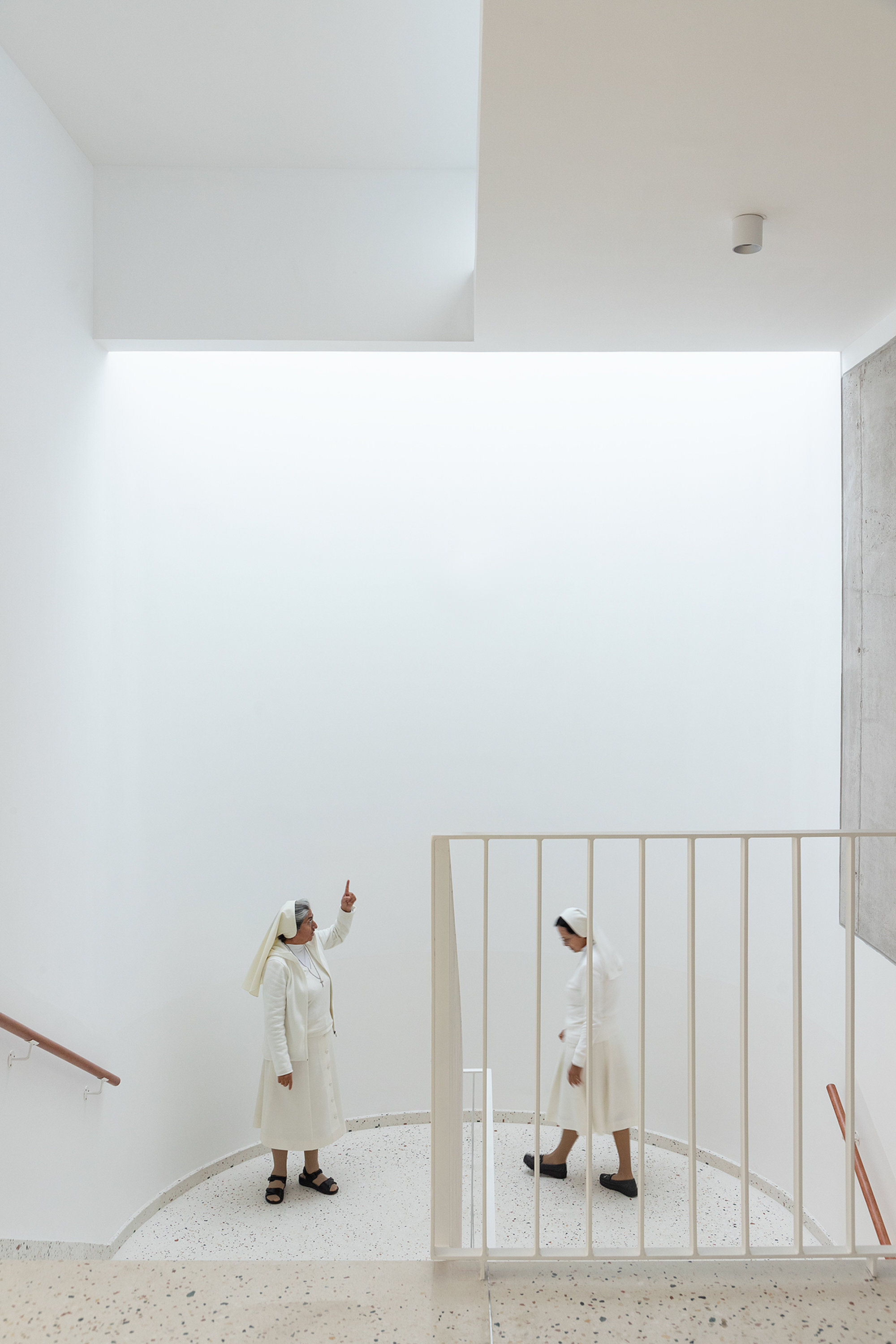 Double-height interior with a curved white balustrade and a person pointing upward in natural light