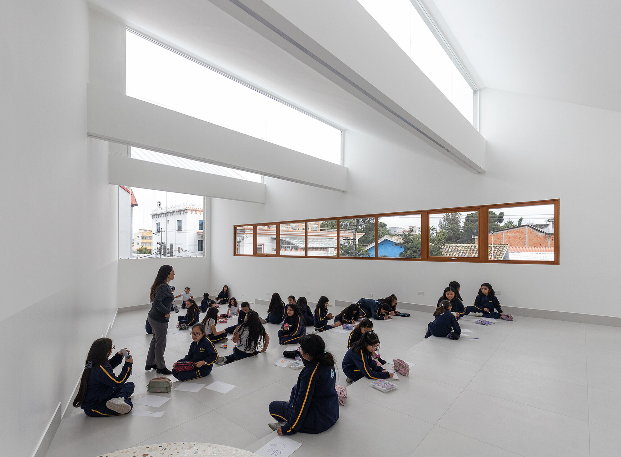 Classroom with continuous timber-framed ribbon windows where students sit on the grey tile floor