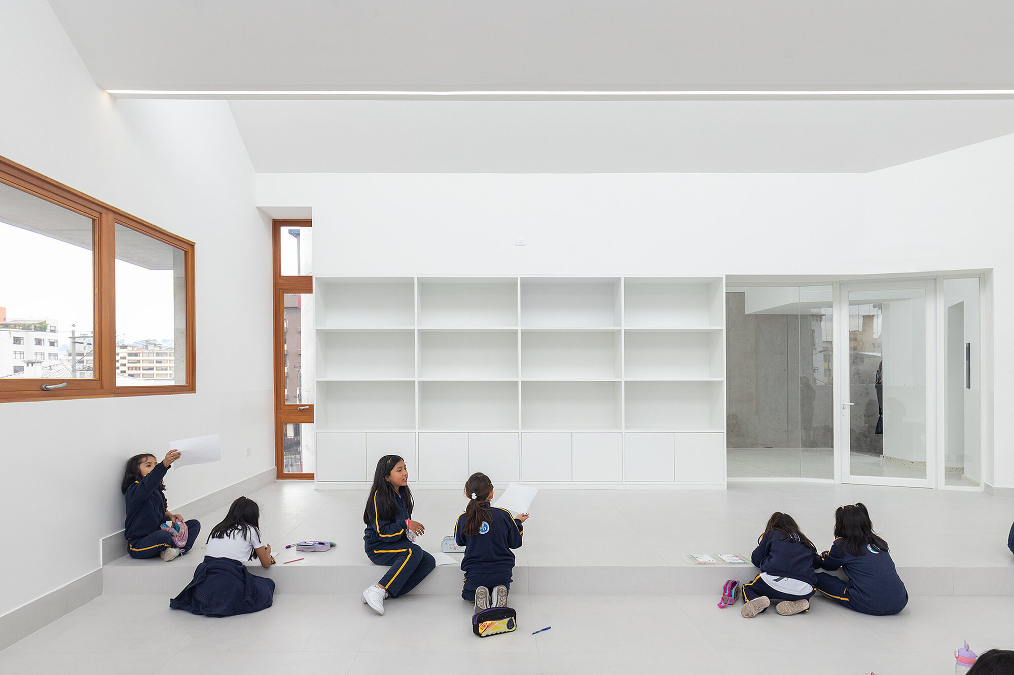 Classroom with built-in white shelving and timber-framed windows as students gather on the floor