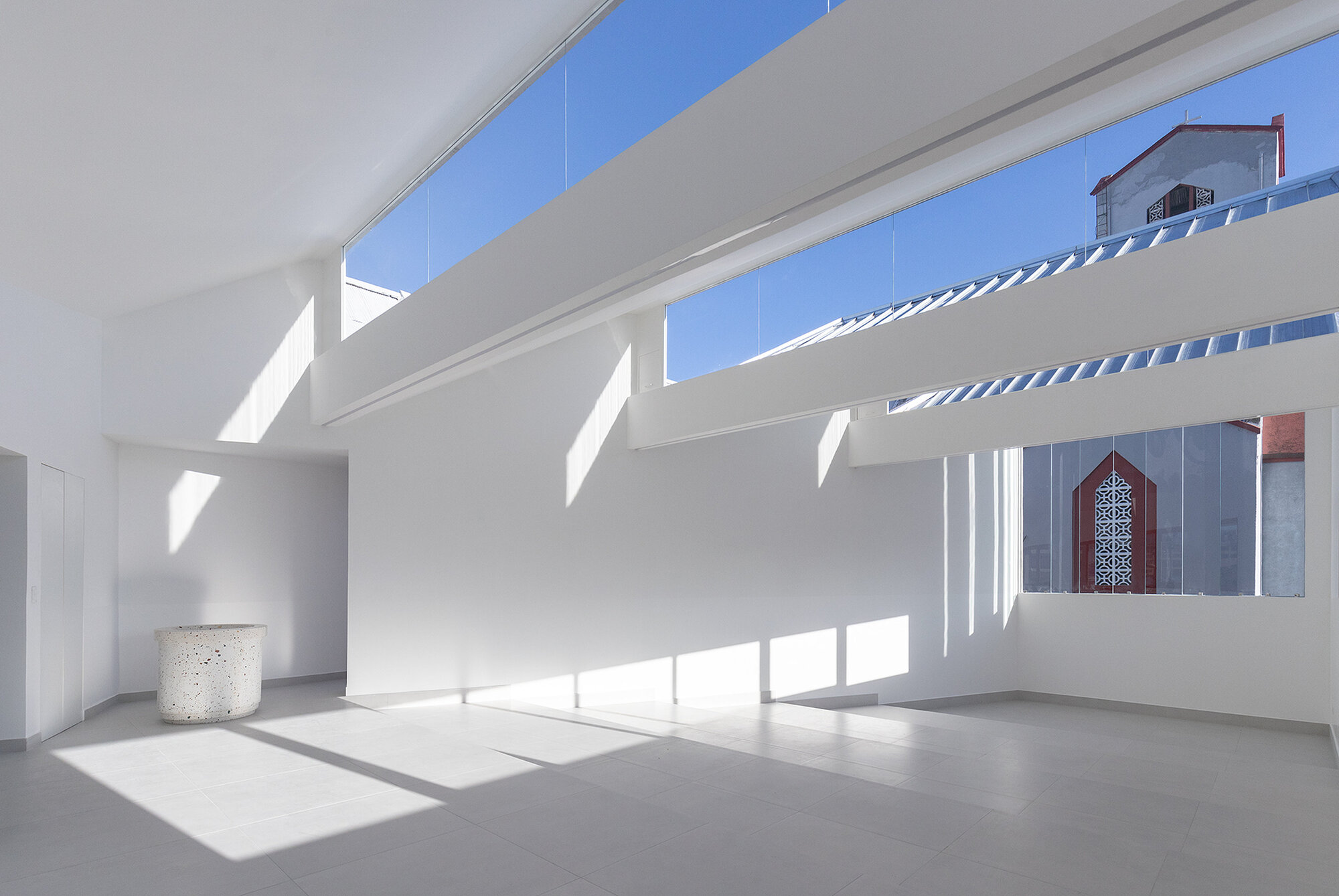 White interior terrace with clerestory windows casting sharp shadows across polished concrete floors