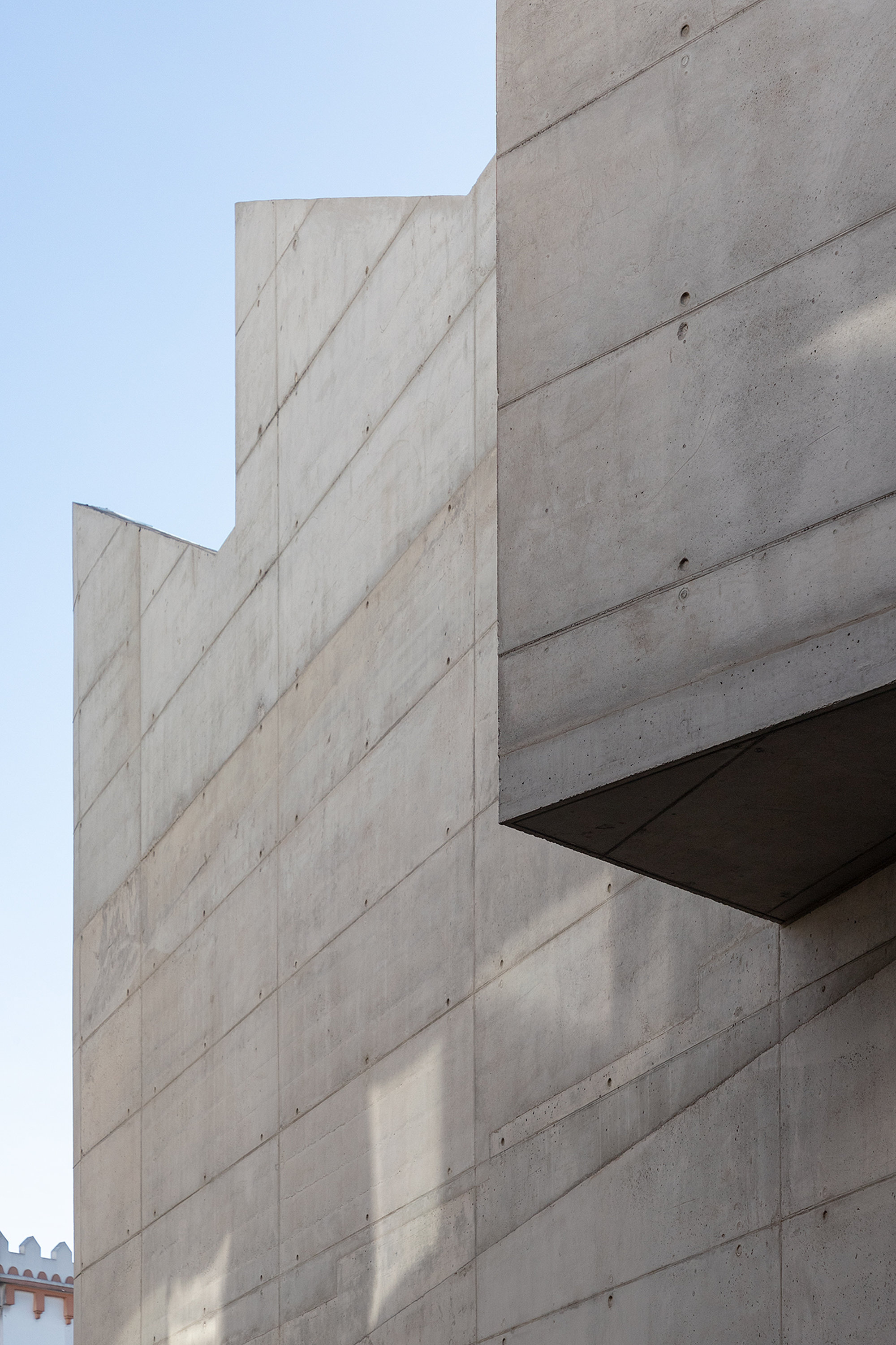 Stepped board-formed concrete facade showing panel joints and formwork tie holes