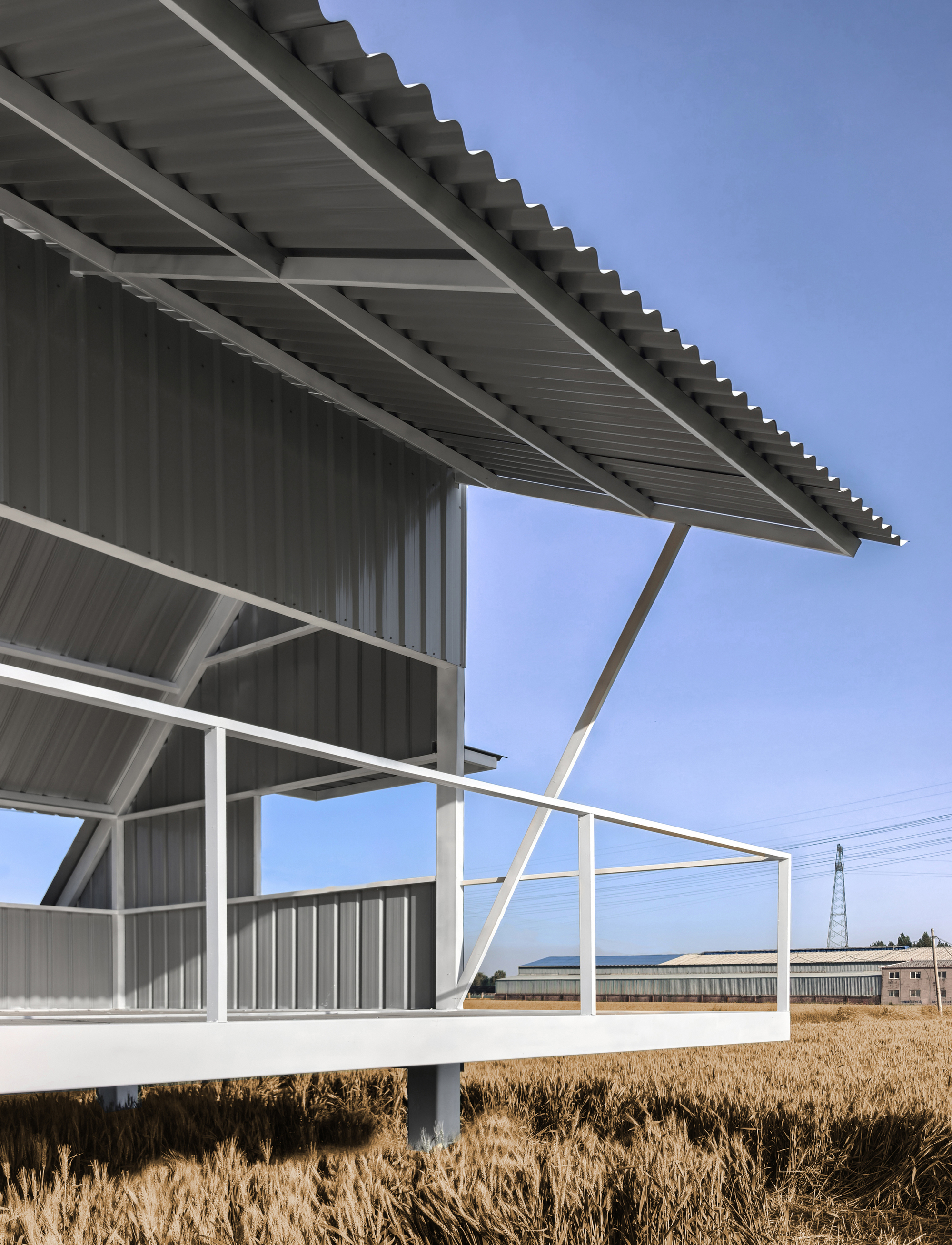 Elevated walkway with white steel railings and corrugated metal canopy overlooking a harvested wheat field