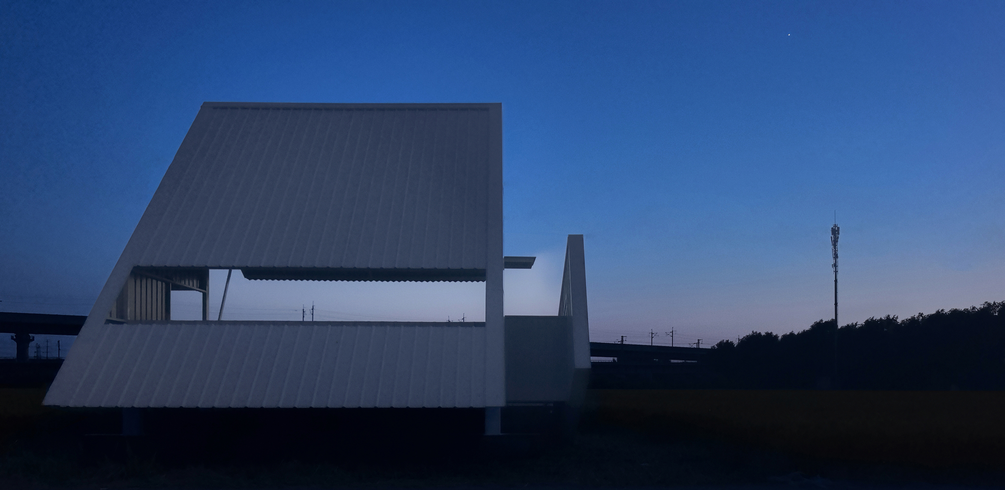 Corrugated metal tower and angled canopy photographed at twilight with transmission tower in distance
