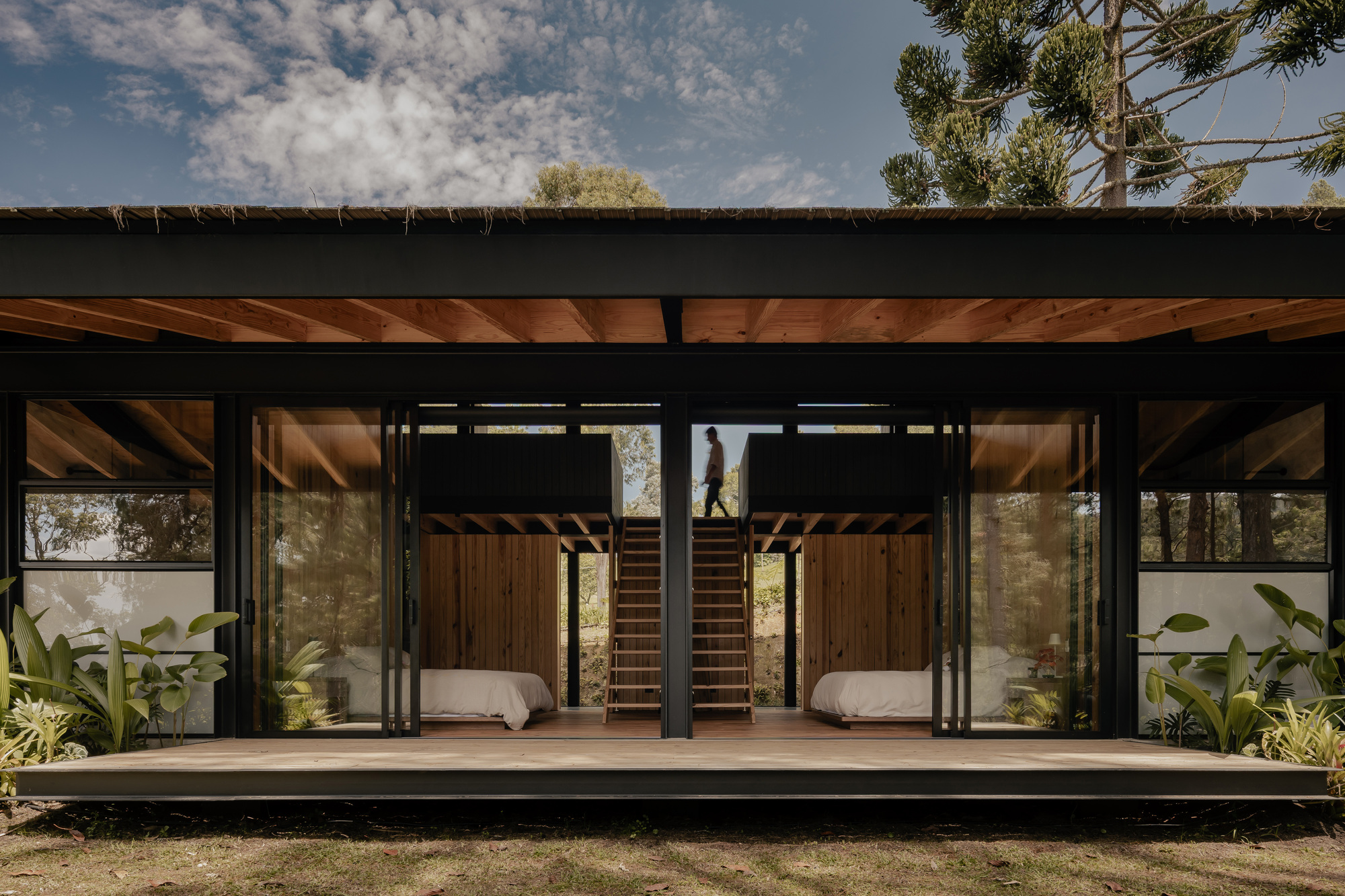 Front elevation showing sliding glass doors and central staircase beneath exposed timber ceiling beams and black steel frame
