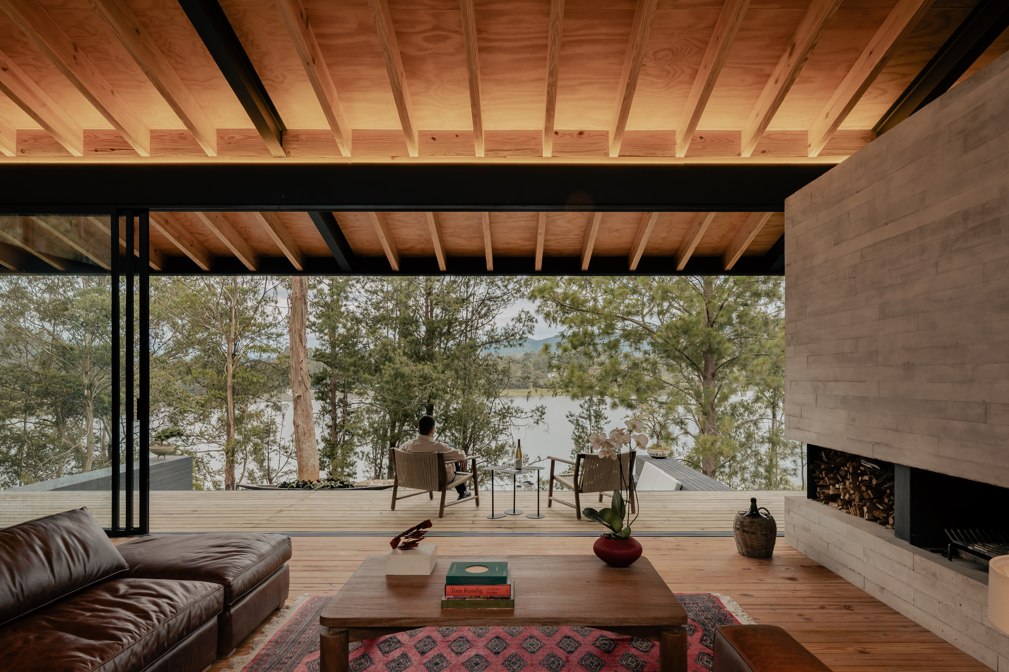 View from seating area through steel-framed glazing toward the outdoor terrace and water beyond