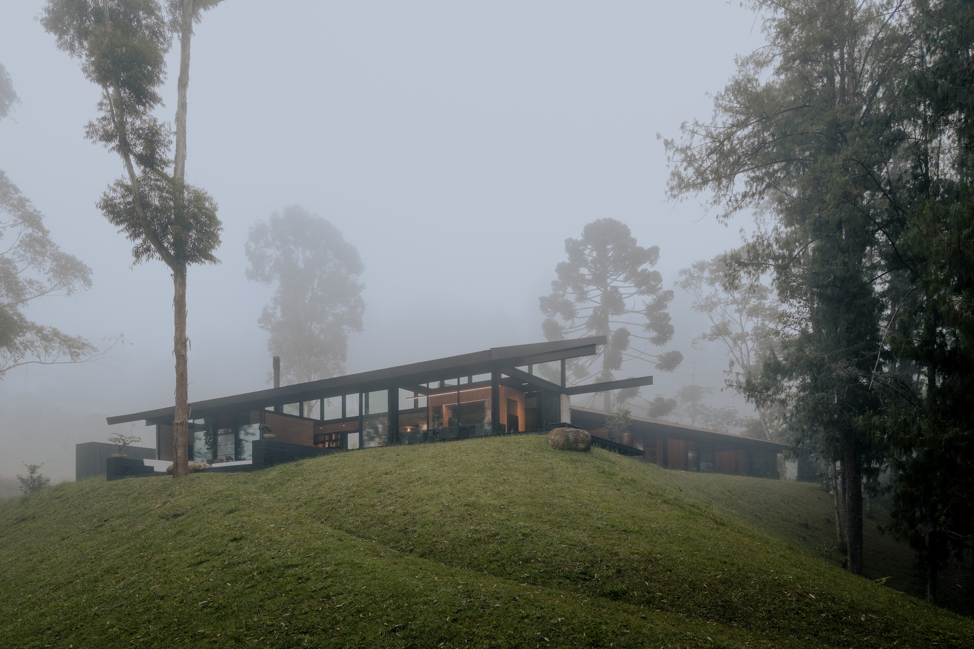 Hillside pavilion with extended flat roof and glazed walls emerging from dense fog