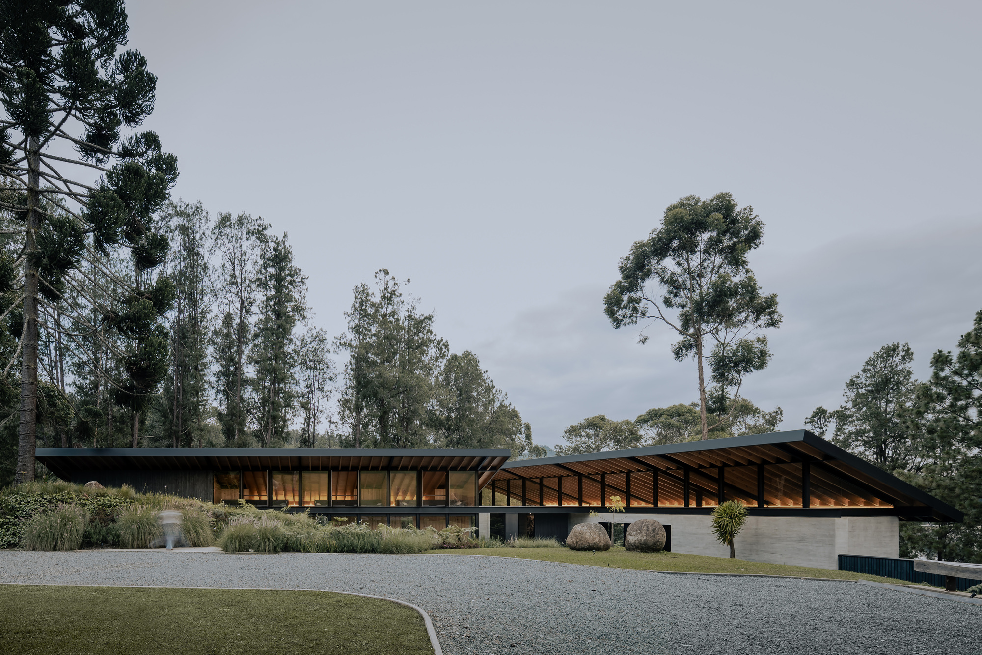 Entry approach showing the sloped roof canopy over timber-clad and glazed facades at dusk