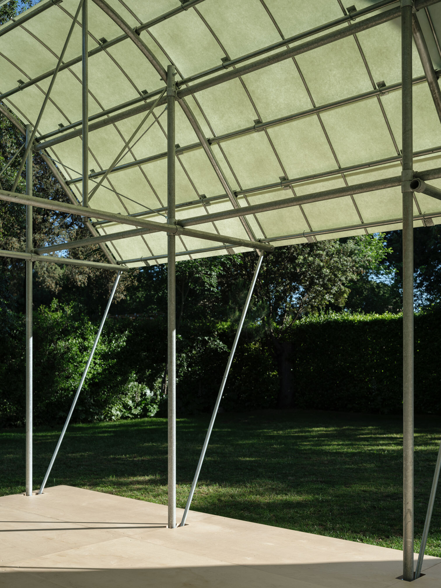 View beneath the tensile canopy showing slender angled steel supports and gridded fabric panels filtering daylight