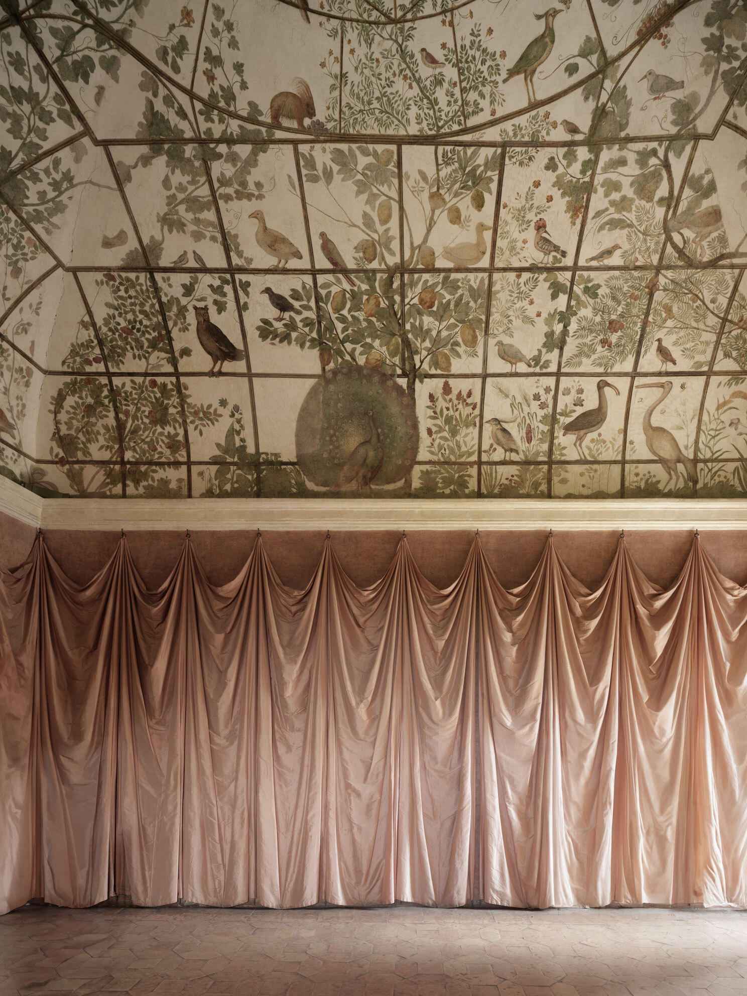 Interior room with botanical wallpaper ceiling showing birds and foliage above draped pink curtain wall
