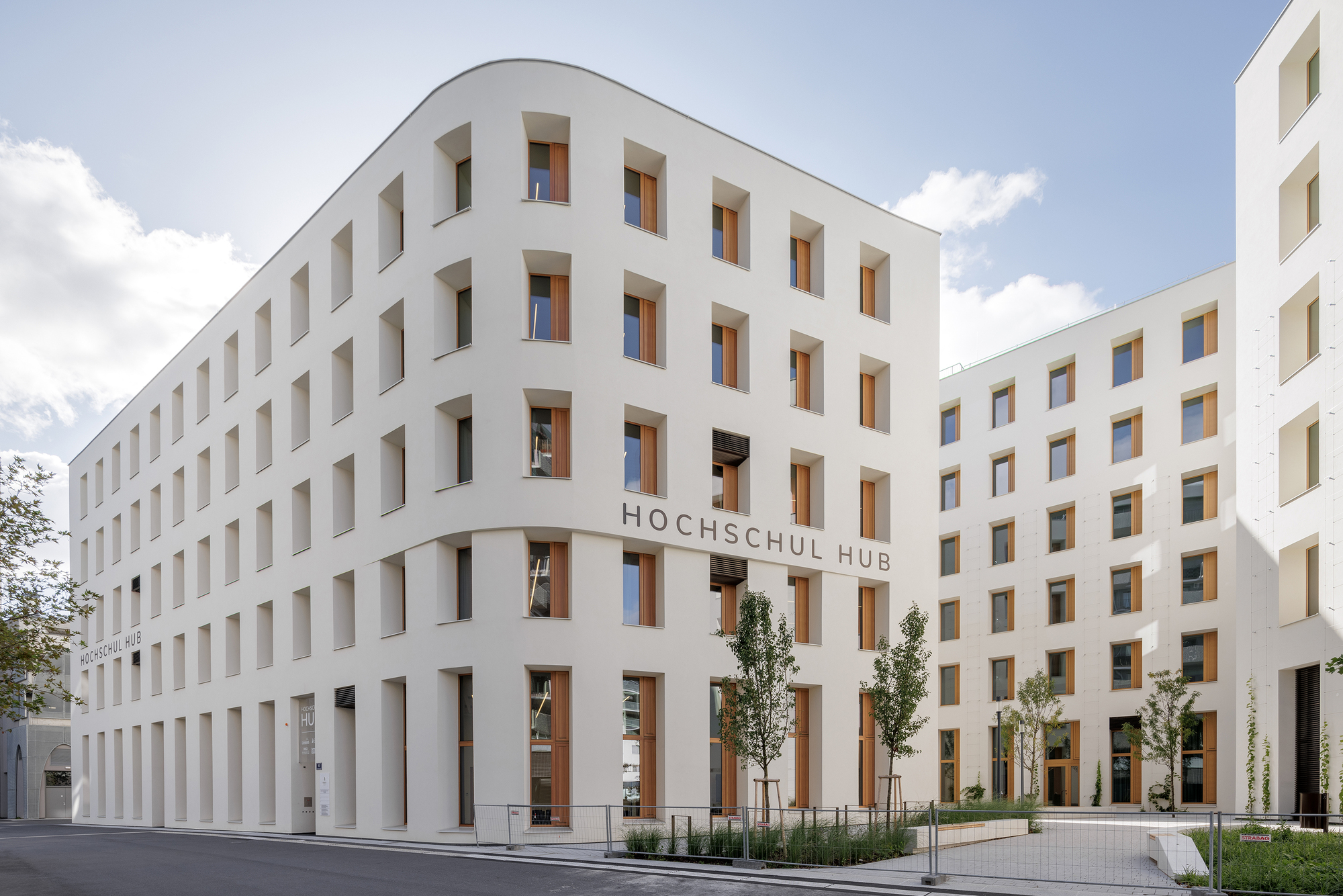 White facade with deep-set timber-lined windows and a ground-level colonnade framing a planted courtyard