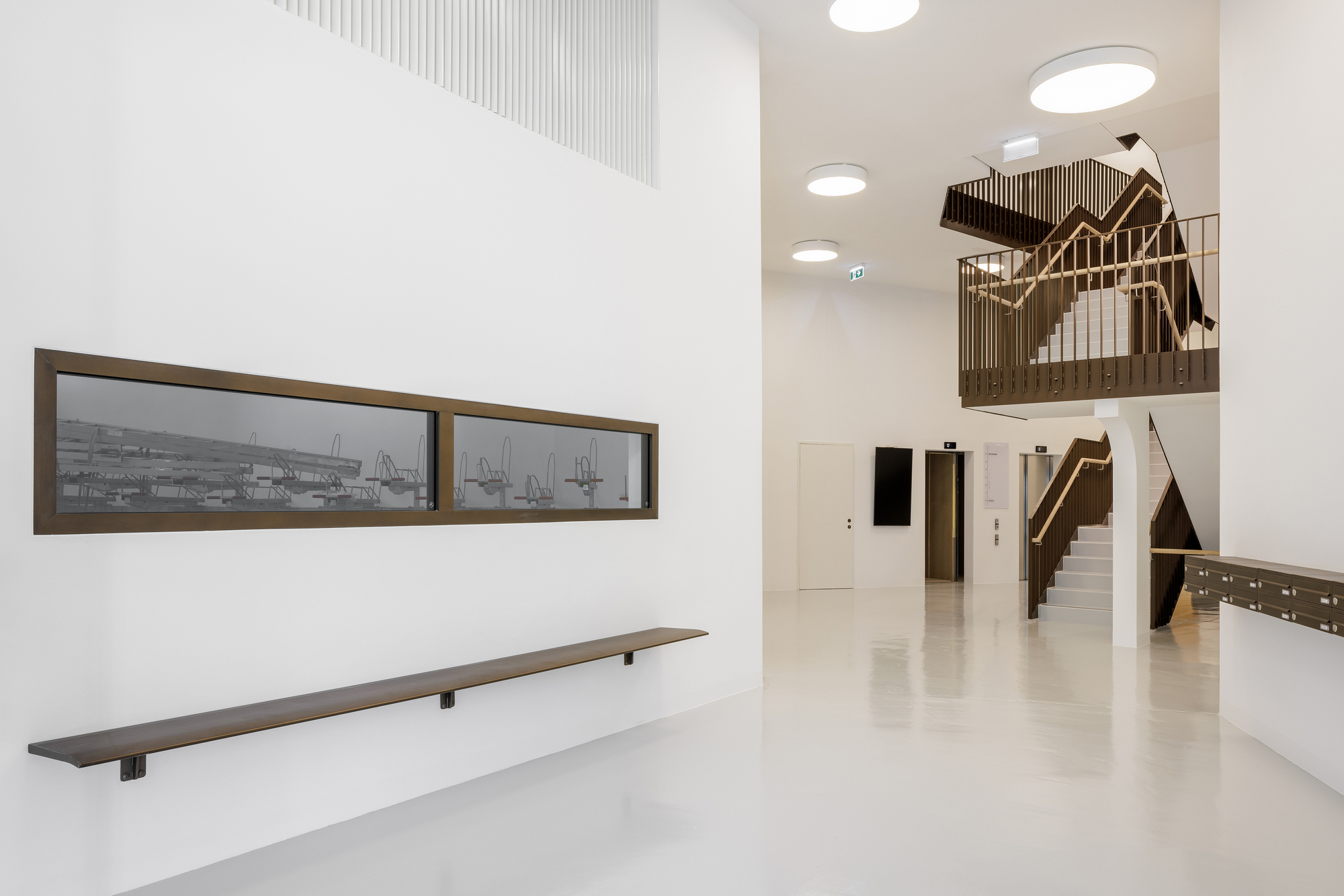 Double-height lobby with a timber-clad staircase and circular ceiling lights above polished flooring