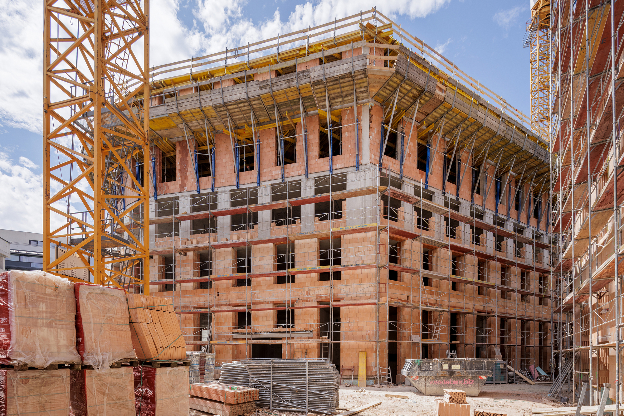 Construction site view of the terracotta block structure with timber framing under yellow tower cranes
