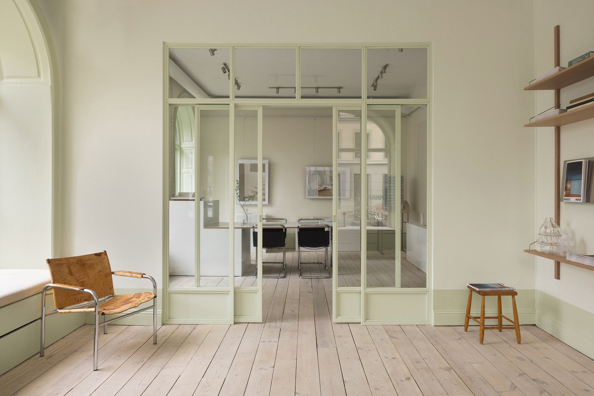 View through a pale green gridded glass partition into a dining area with light wooden floorboards