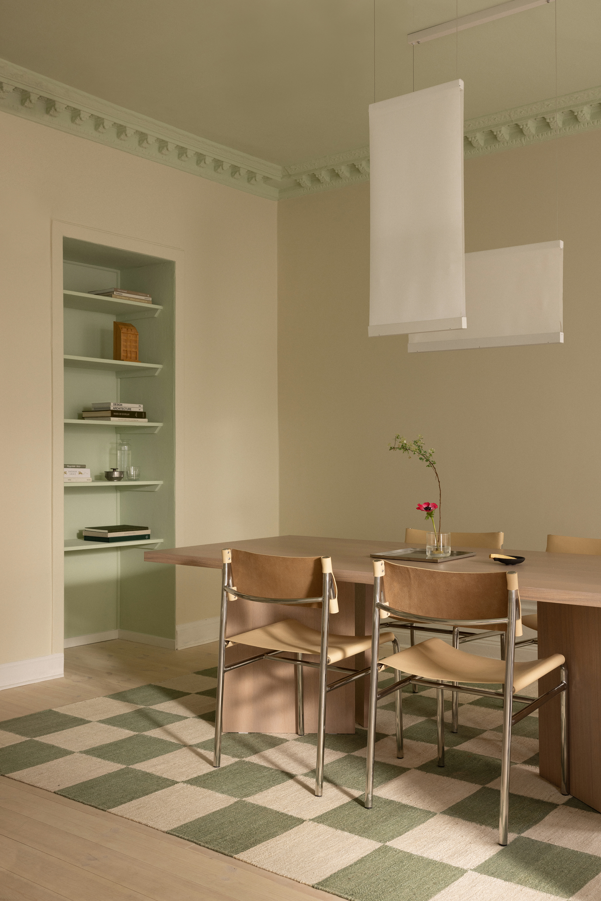 Dining area with checkered cream and green floor tiles beneath a white pendant lamp and decorative cornice