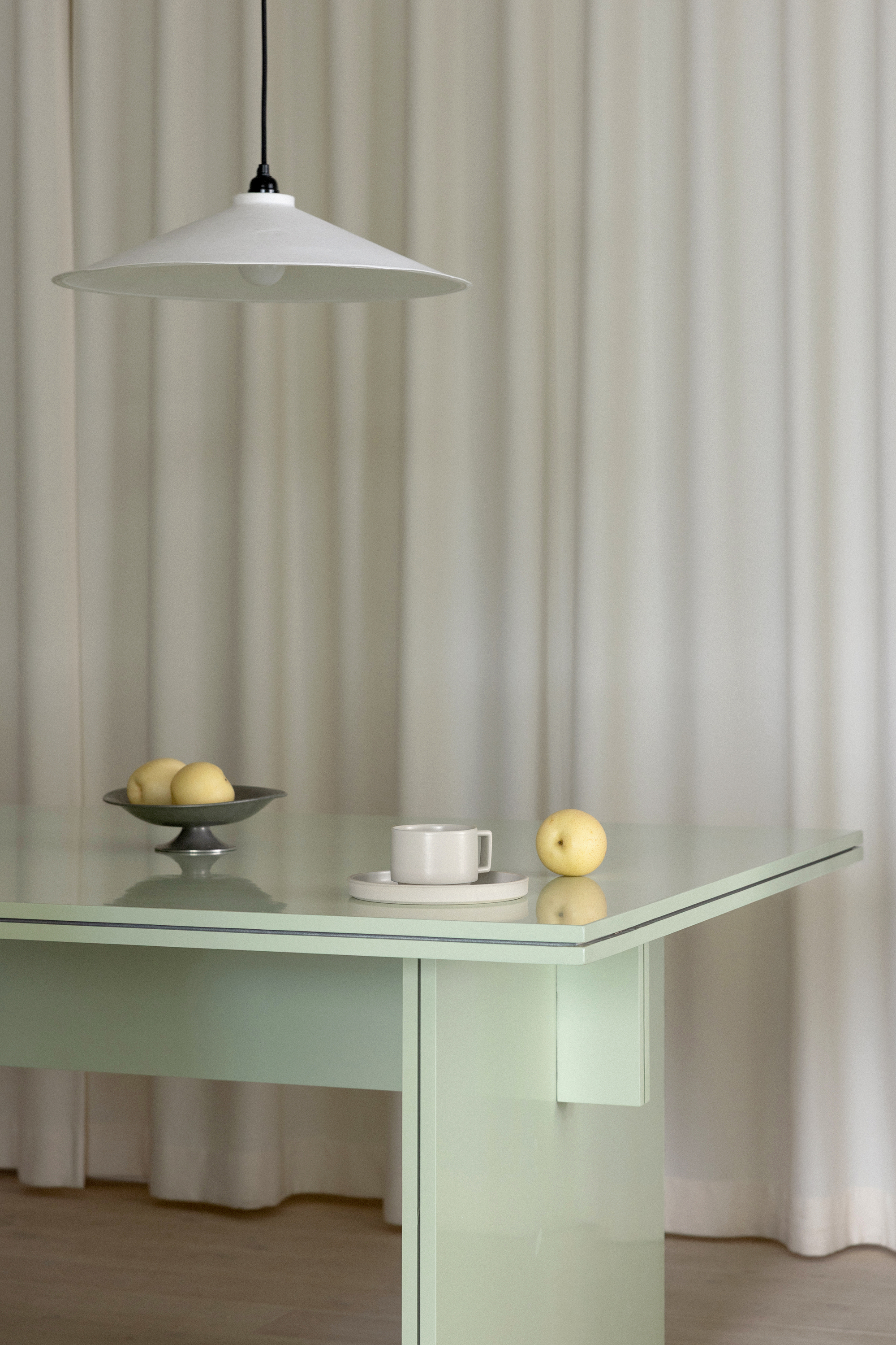 Glass-topped table in pale green with white conical pendant light and ceramic fruit arrangement