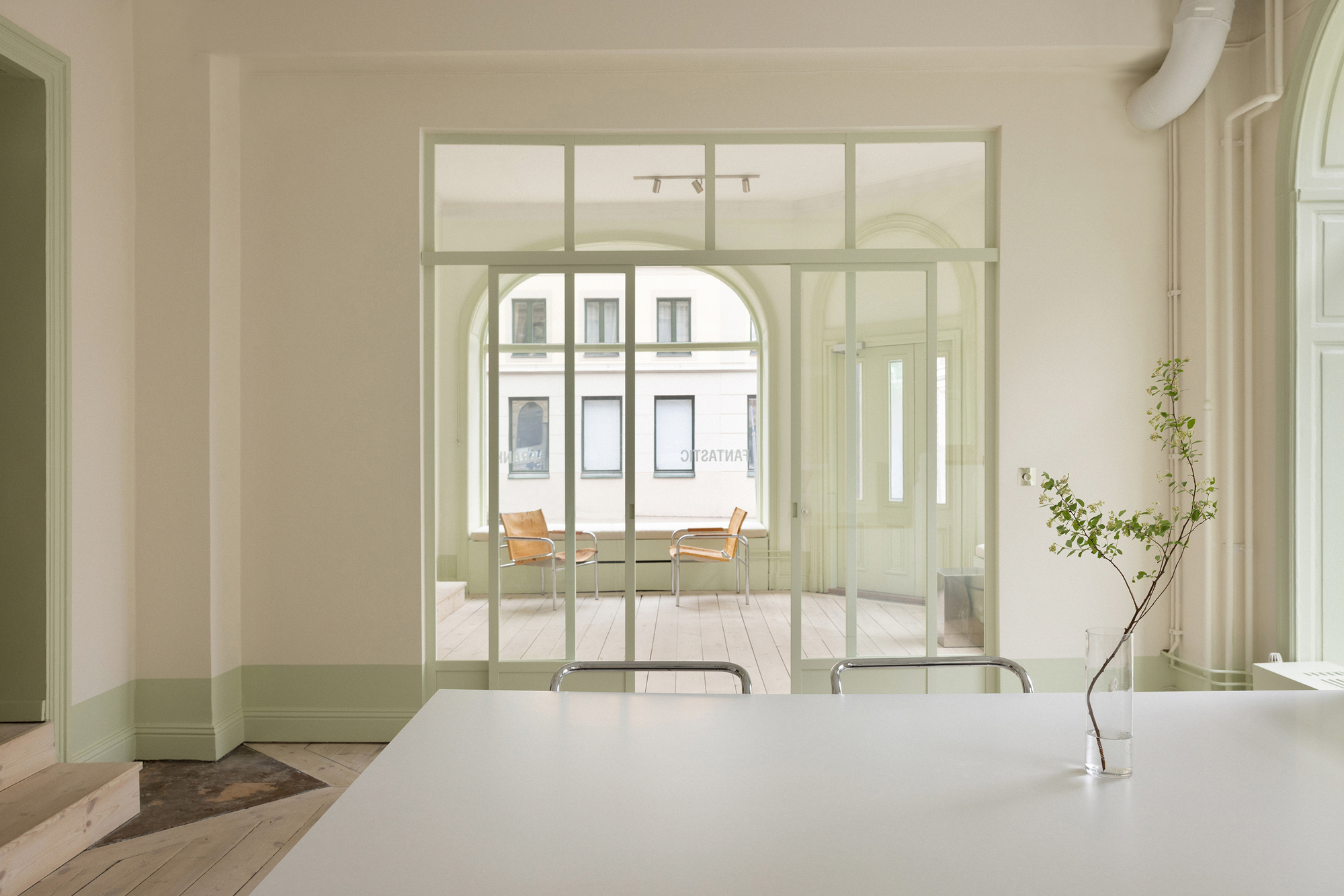 View through pale green steel-framed glass doors into a room with herringbone parquet flooring