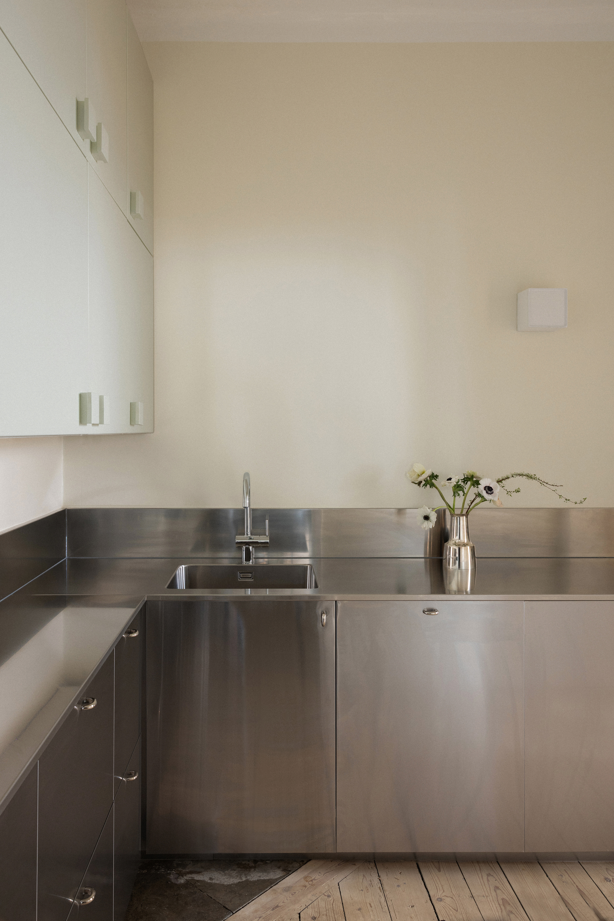 Corner kitchen with brushed stainless steel countertops and cabinetry over wide plank timber flooring