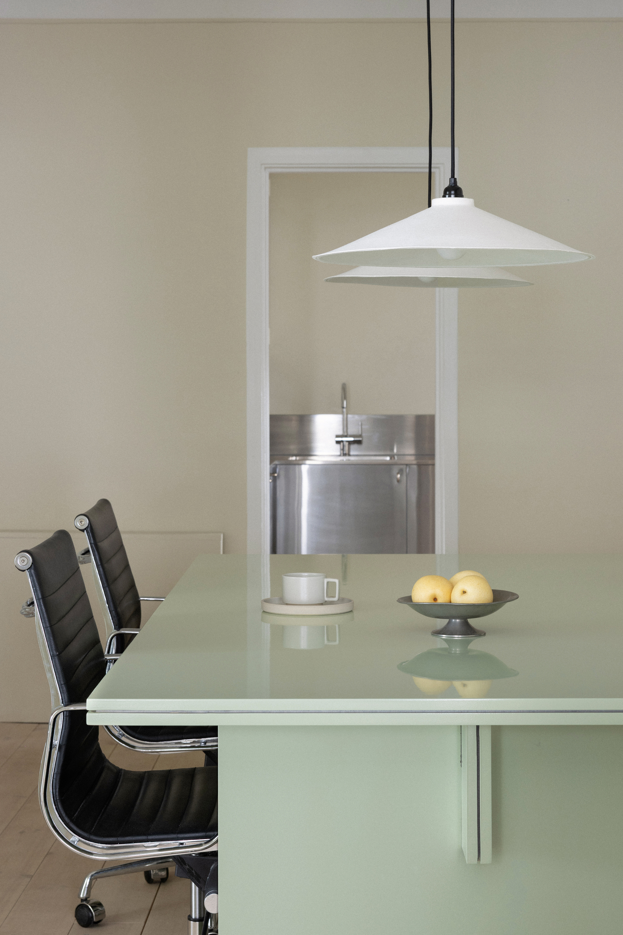 Glass dining table with white pendant lamp and a view through to the stainless kitchen