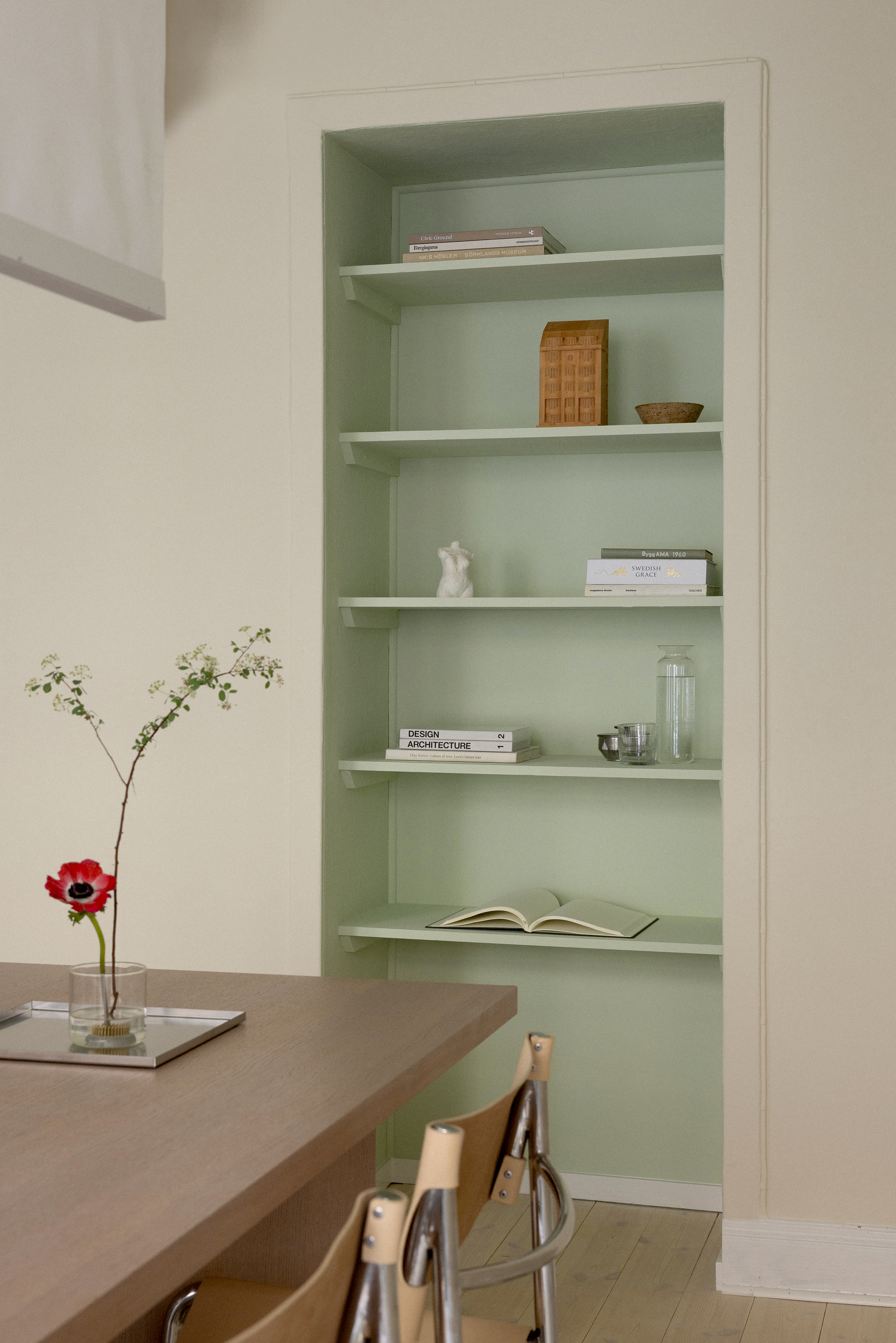 Built-in shelving niche painted pale green with books and objects beside a vase with flowers