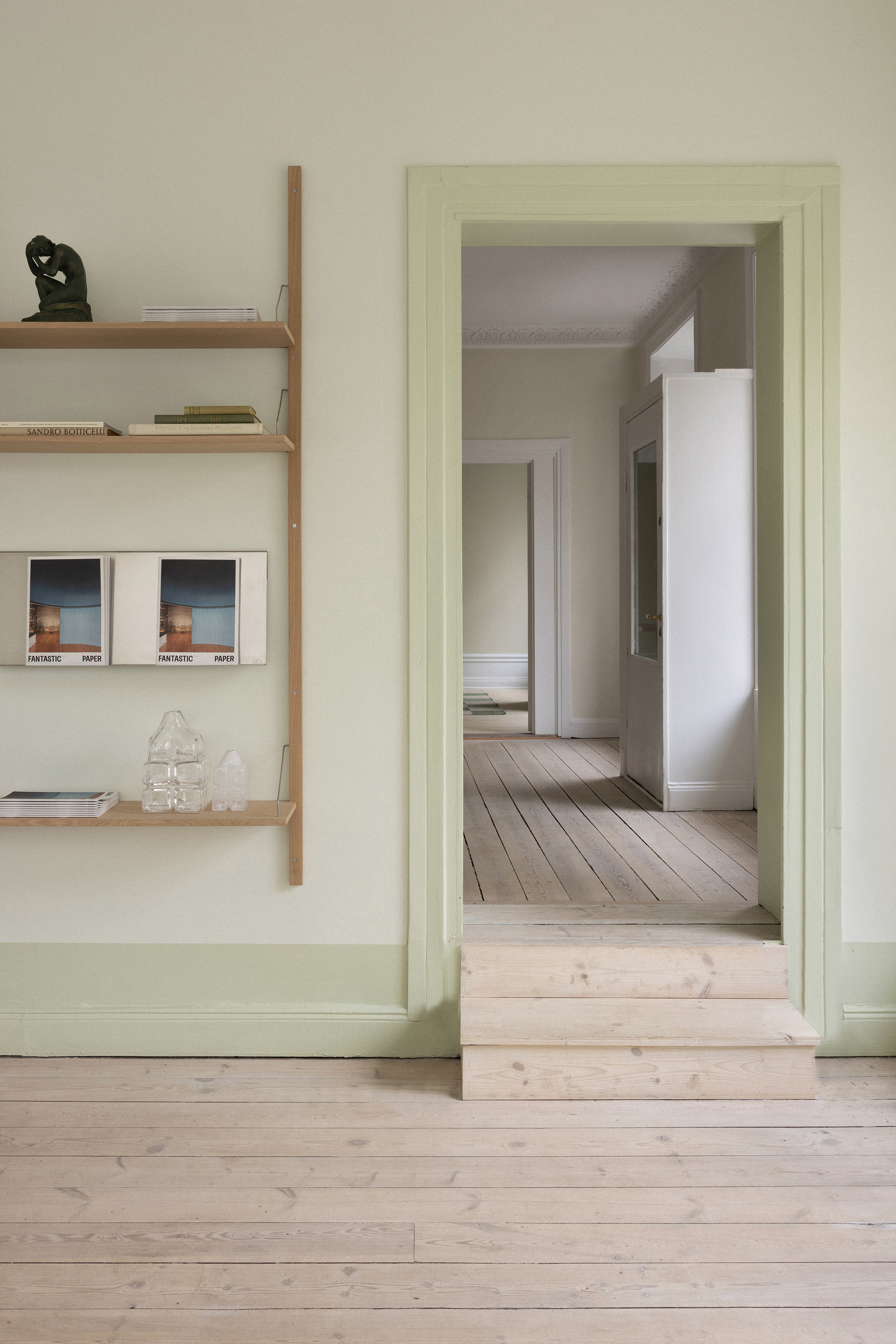 Doorway with pale green trim opening onto a series of aligned rooms with timber floors