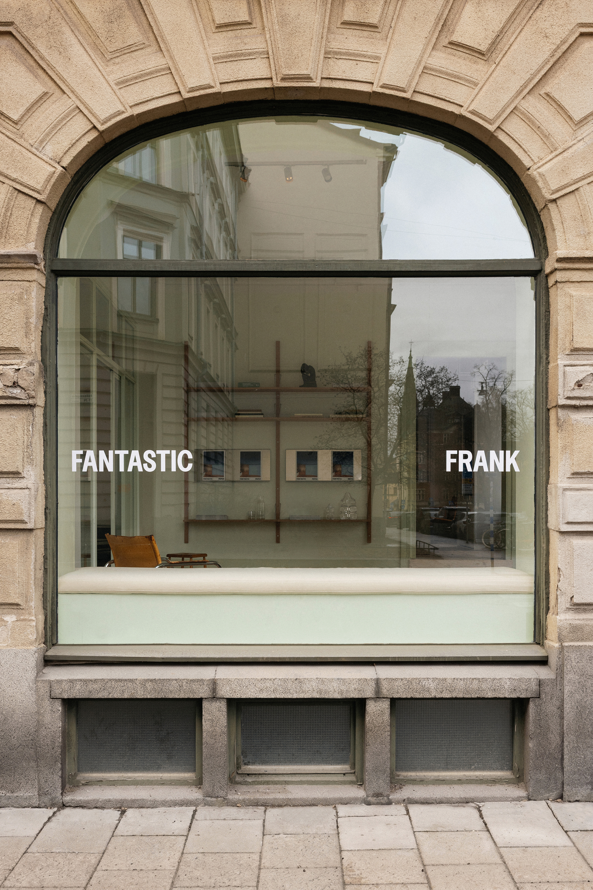 Arched storefront window with black steel frame set within rusticated stone facade under overcast sky