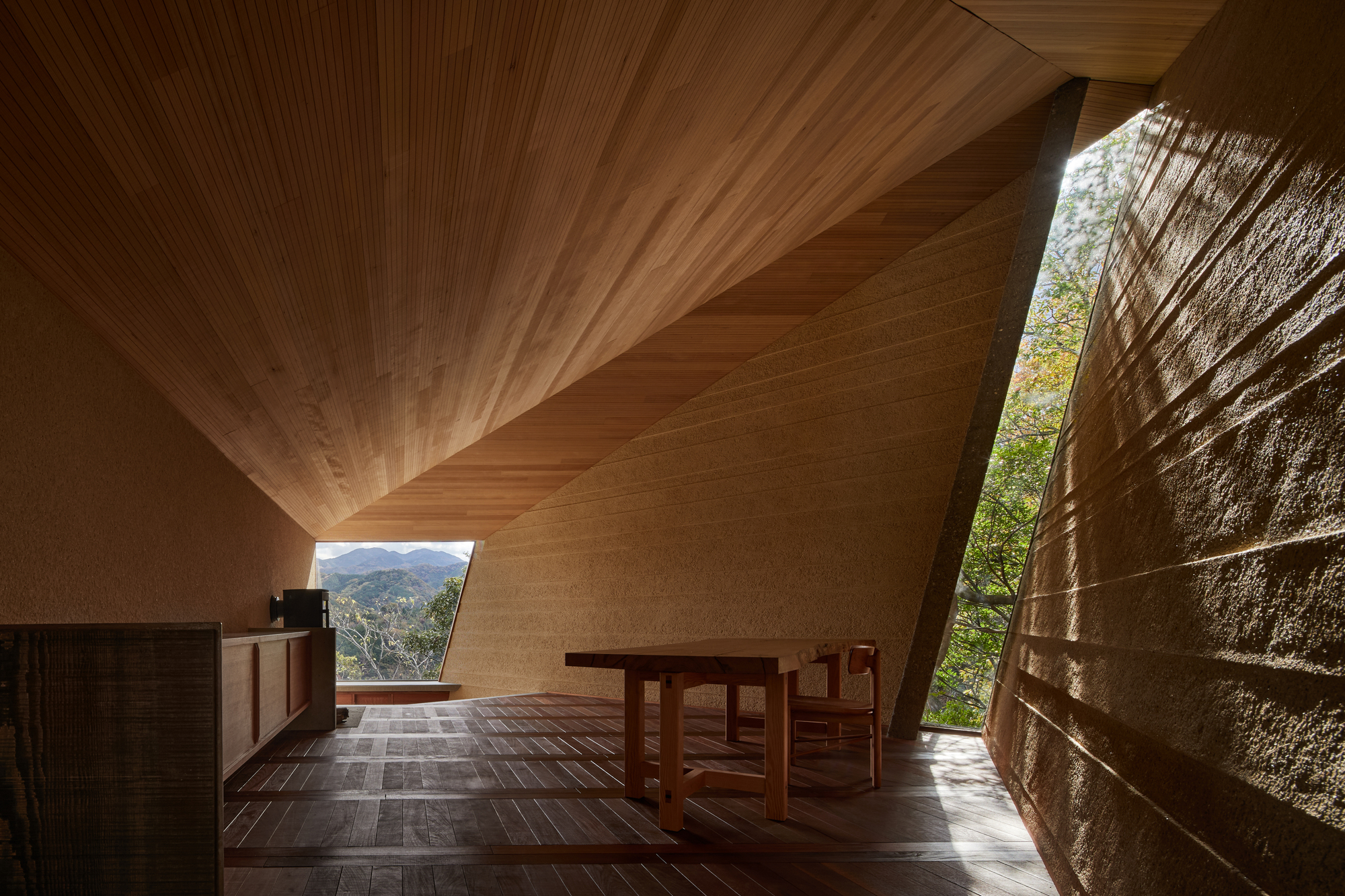 Interior showing ribbed timber ceiling planes converging above stone walls and a framed mountain view