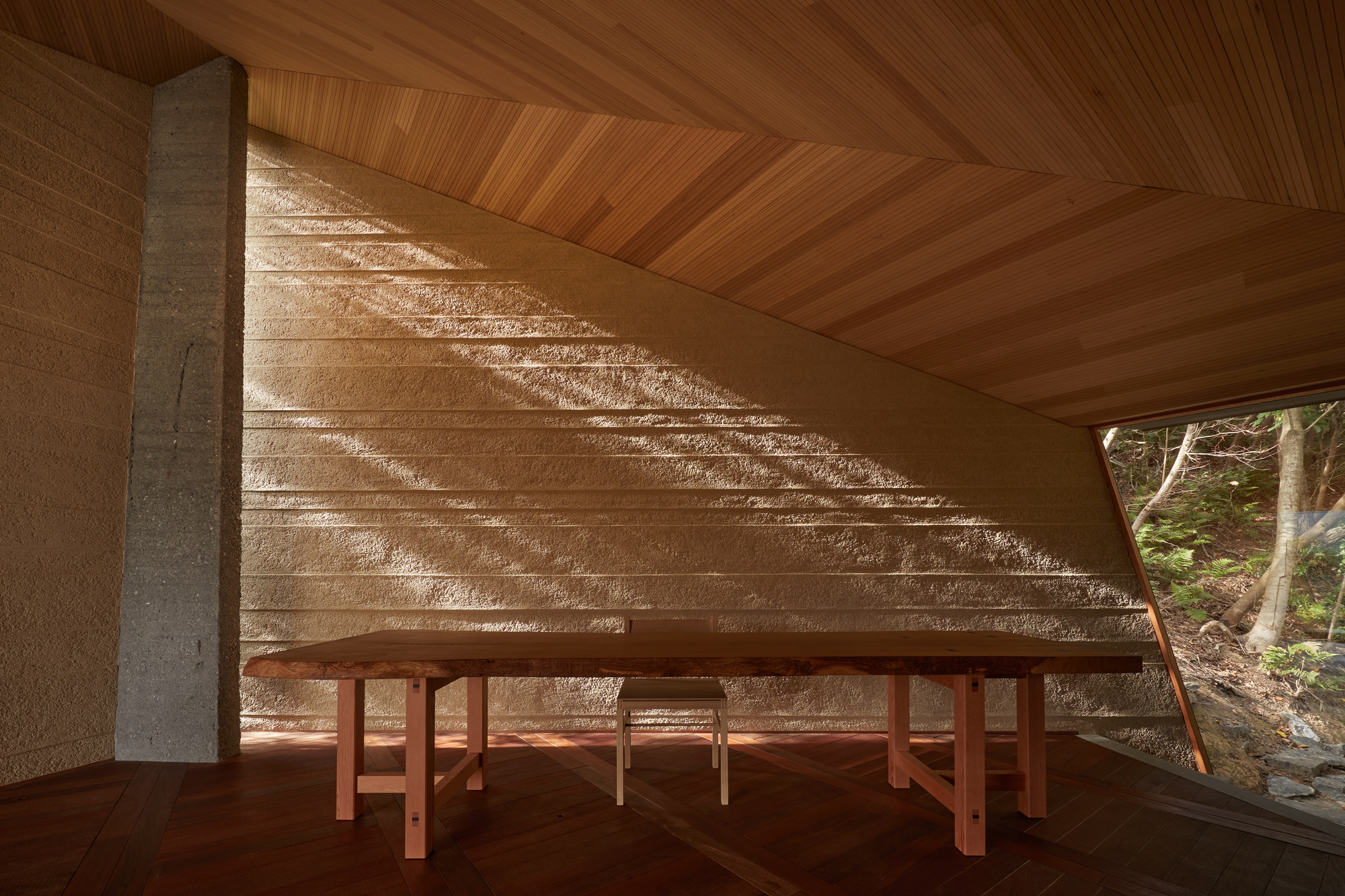 Timber bench against textured stone wall beneath angled ceiling with filtered sunlight