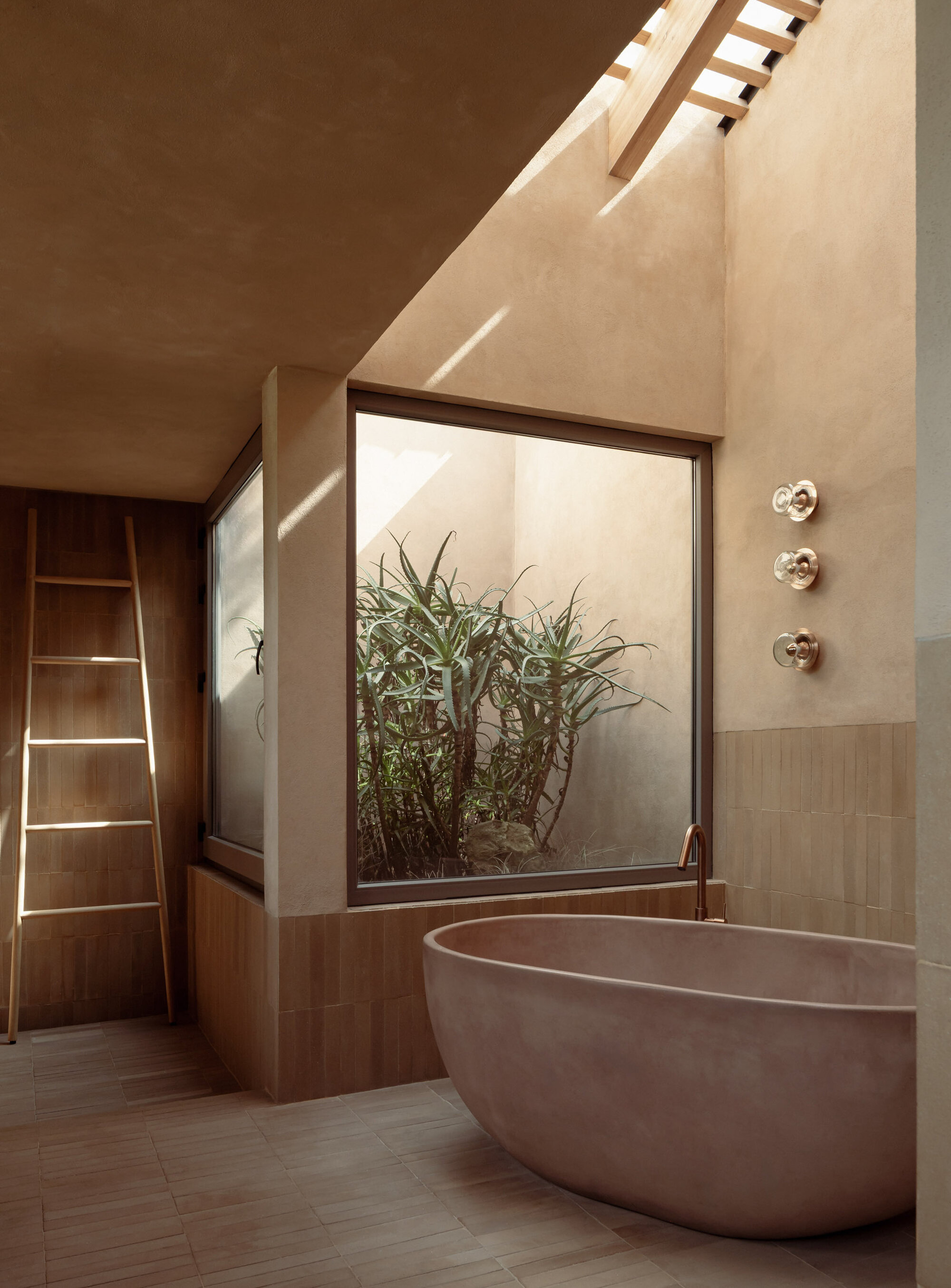 Freestanding bathtub beside a glazed courtyard planted with bamboo beneath a skylit ceiling