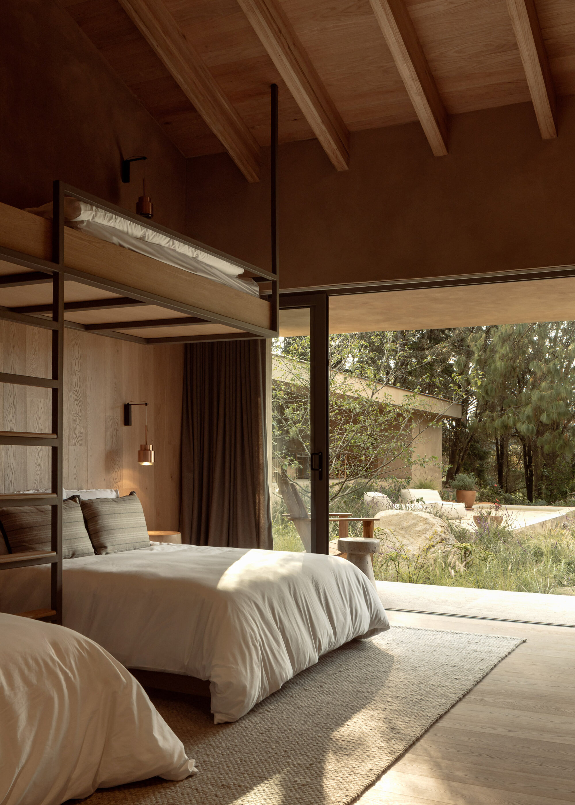 Bedroom with exposed timber ceiling beams and full-height glazing opening to a landscaped garden