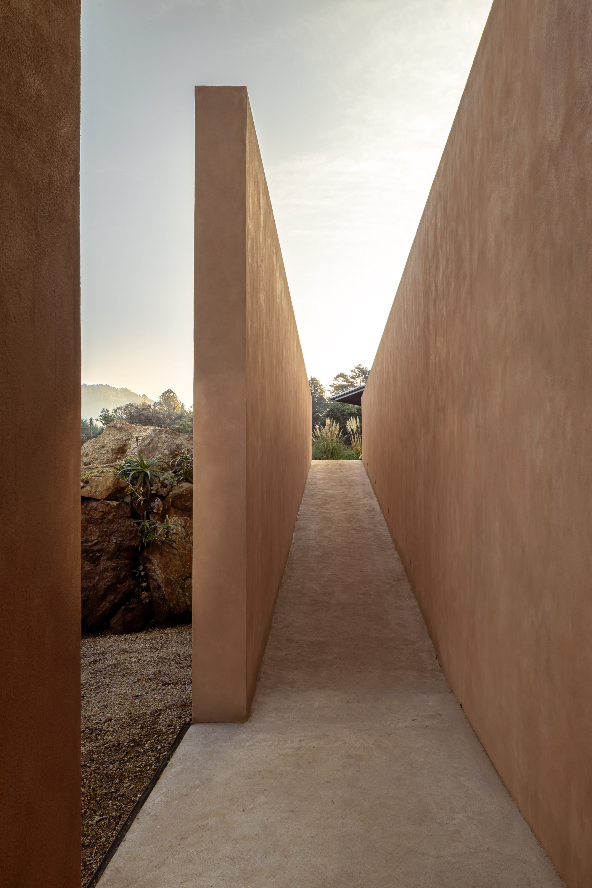 Narrow outdoor corridor between slanted earthen walls under an open sky at dusk