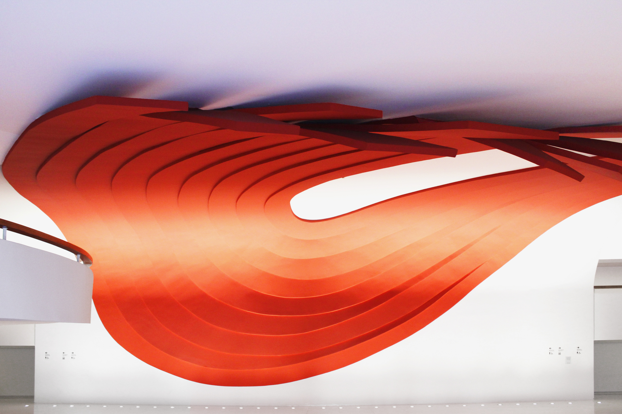 Interior view of the undulating orange ribbed ceiling canopy suspended above a white corridor