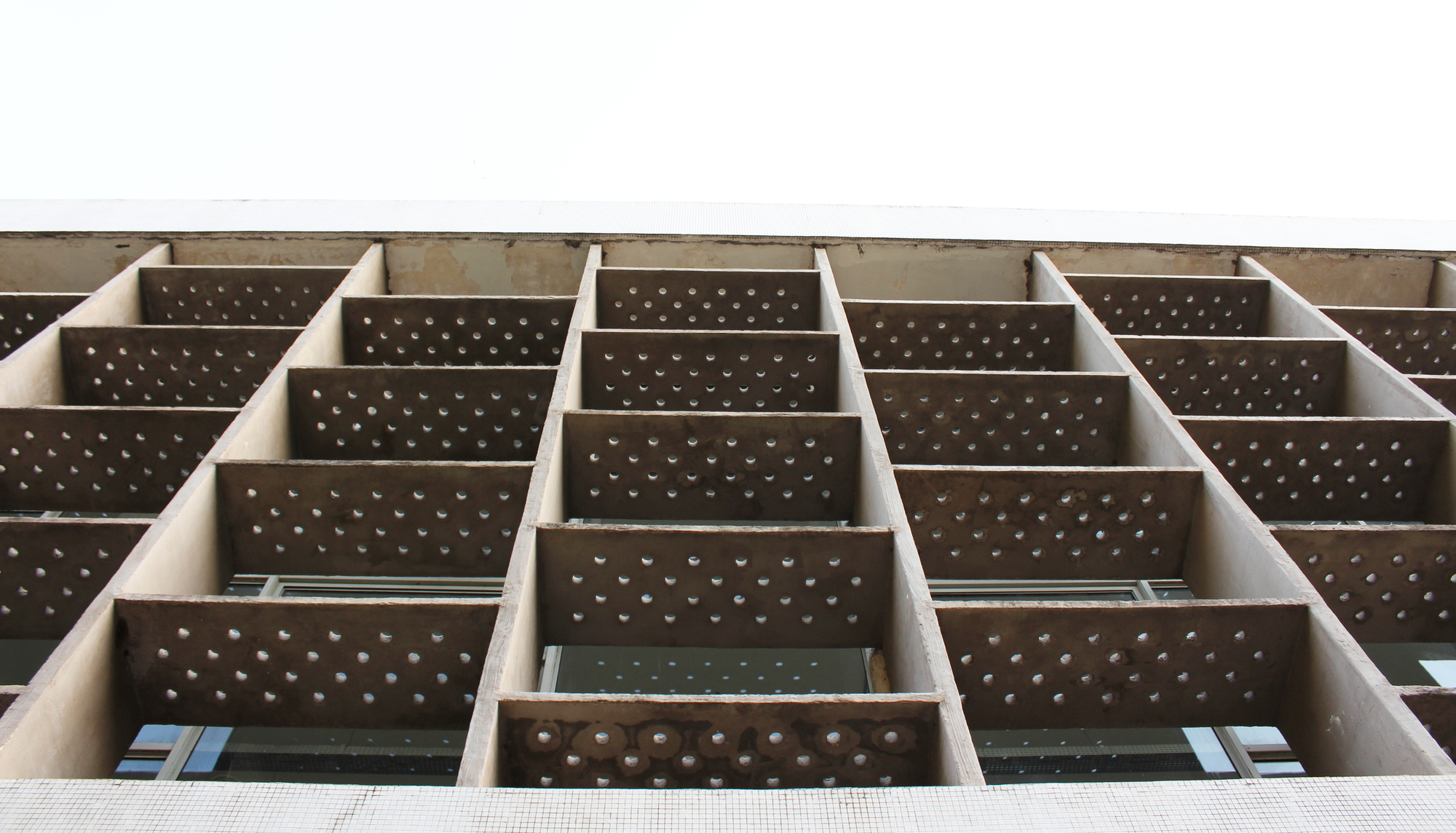 Upward view of the perforated brown panel facade organized in a staggered grid pattern