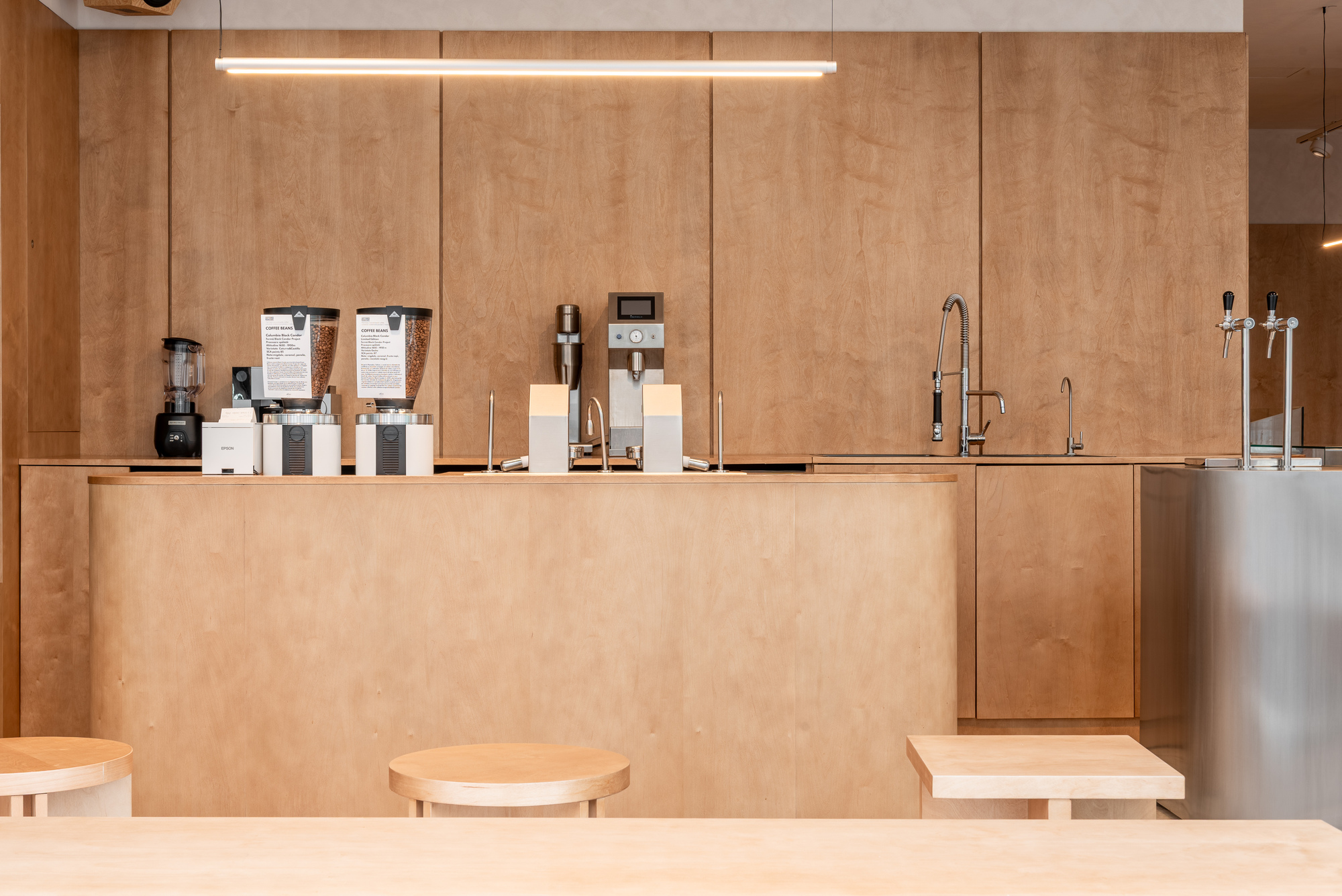 Service counter in plywood with coffee equipment and tap fixtures under linear ceiling lights
