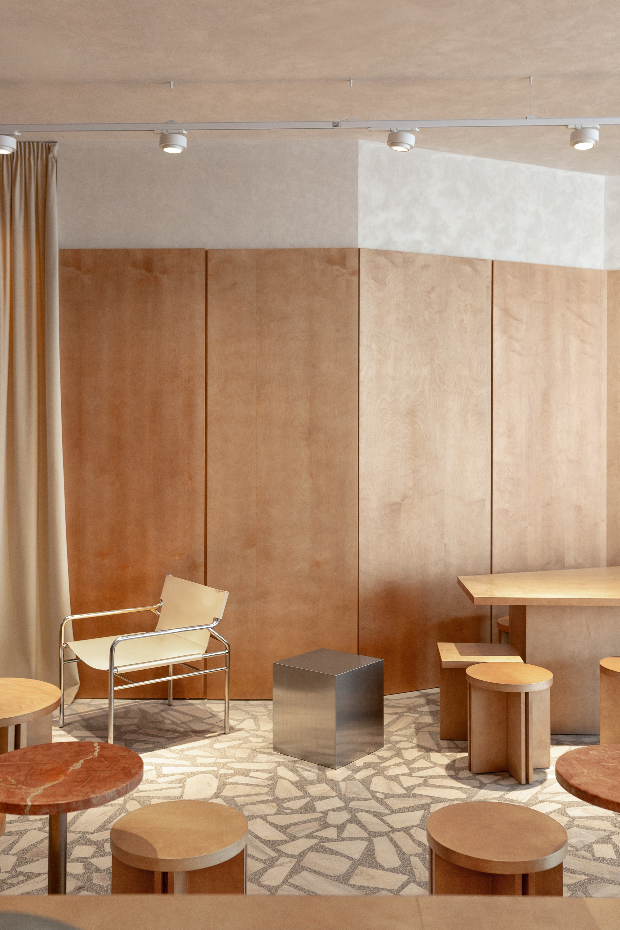 Seating area with plywood wall panels, chrome lounge chair, and terrazzo floor under track lighting