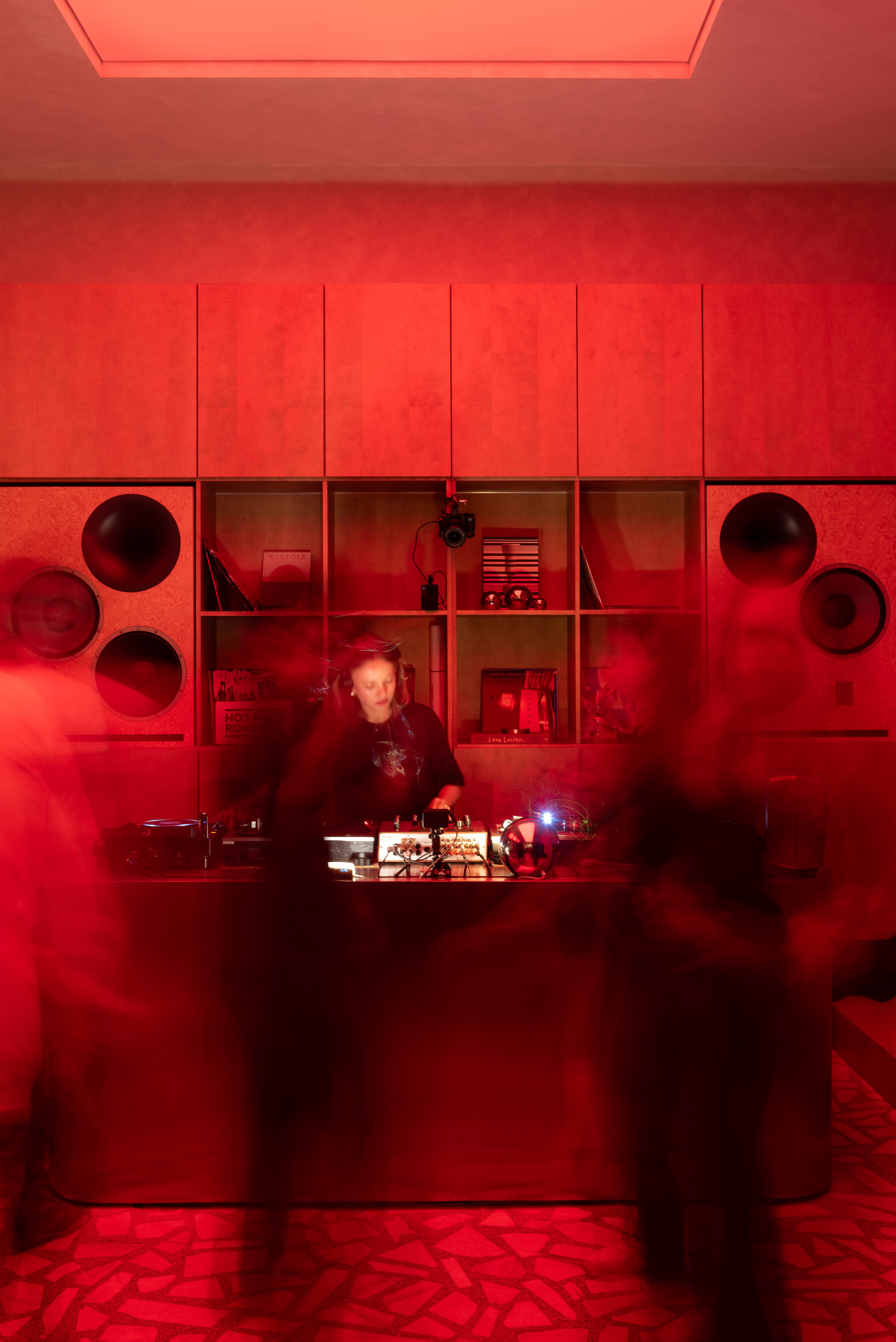 Red-lit service counter with circular openings and shelving units behind a figure working at dusk