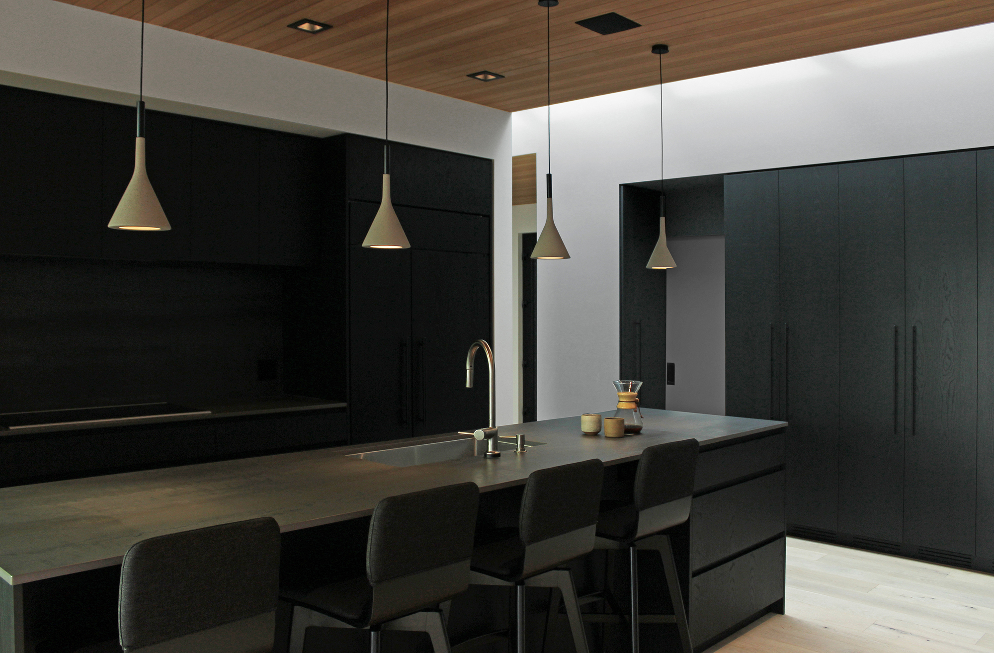 Kitchen island with black cabinetry and brass pendant lights beneath wood ceiling