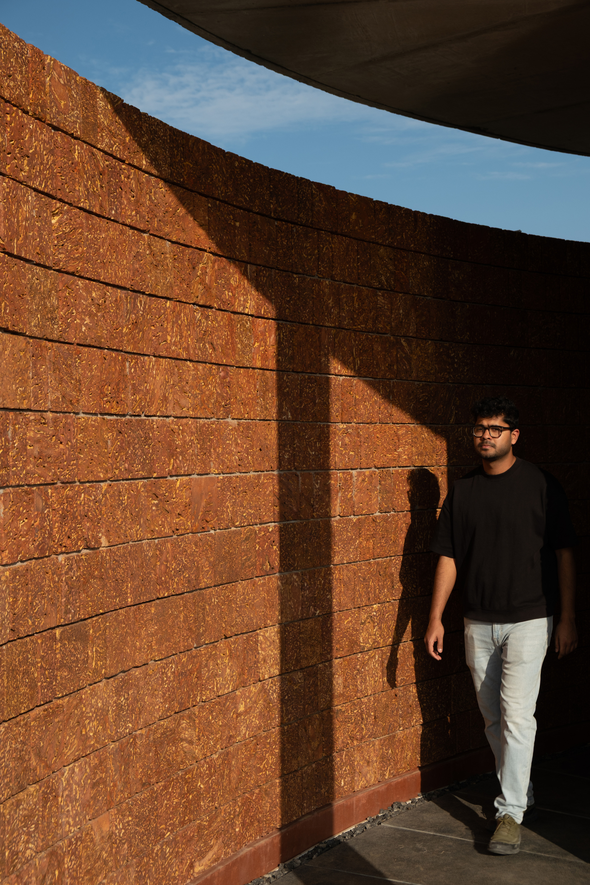 Curved laterite brick wall with vertical shadow pattern as a person walks beneath the overhang