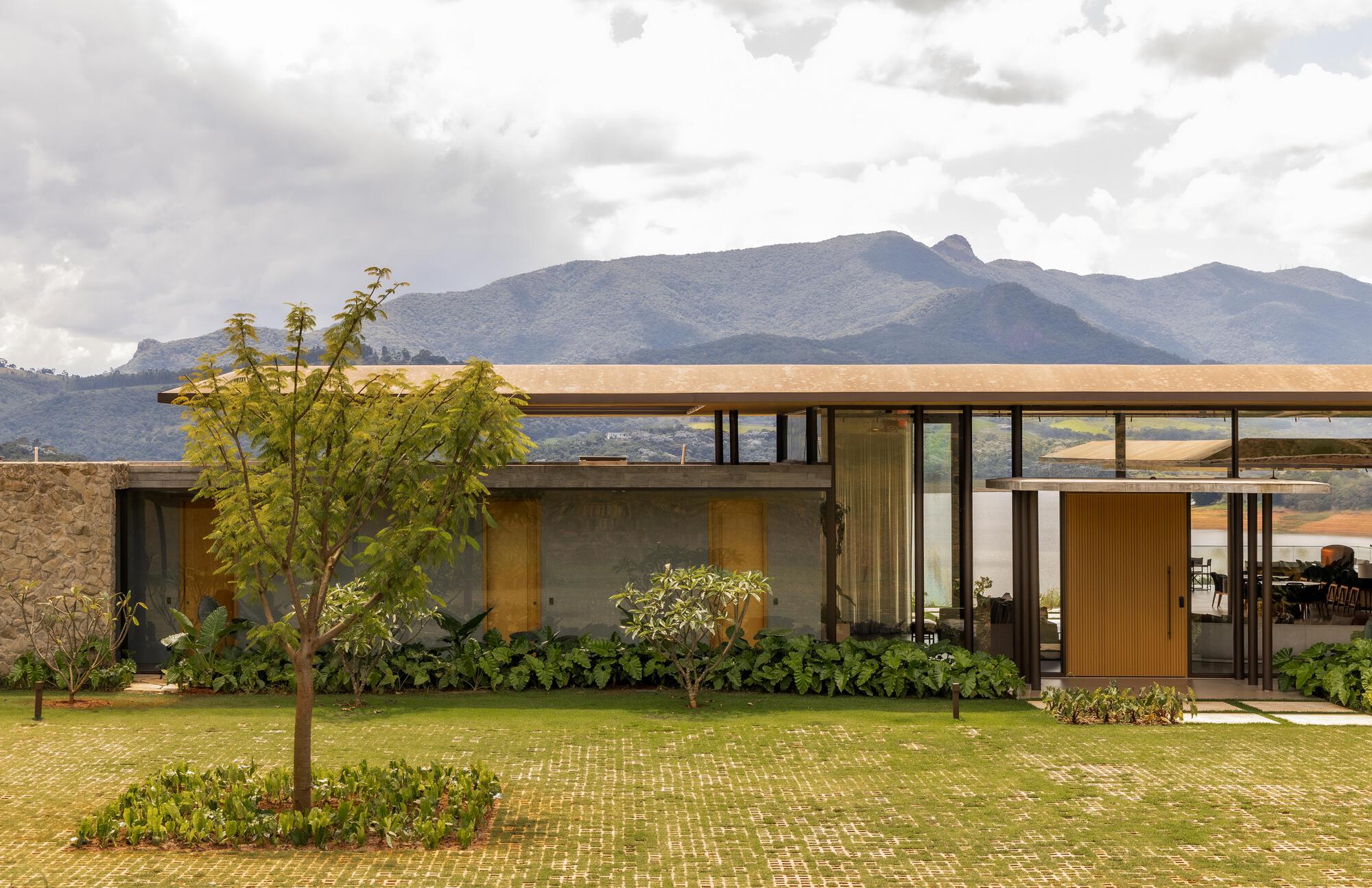 Glass-walled pavilion with overhanging timber roof set against distant mountains under overcast sky