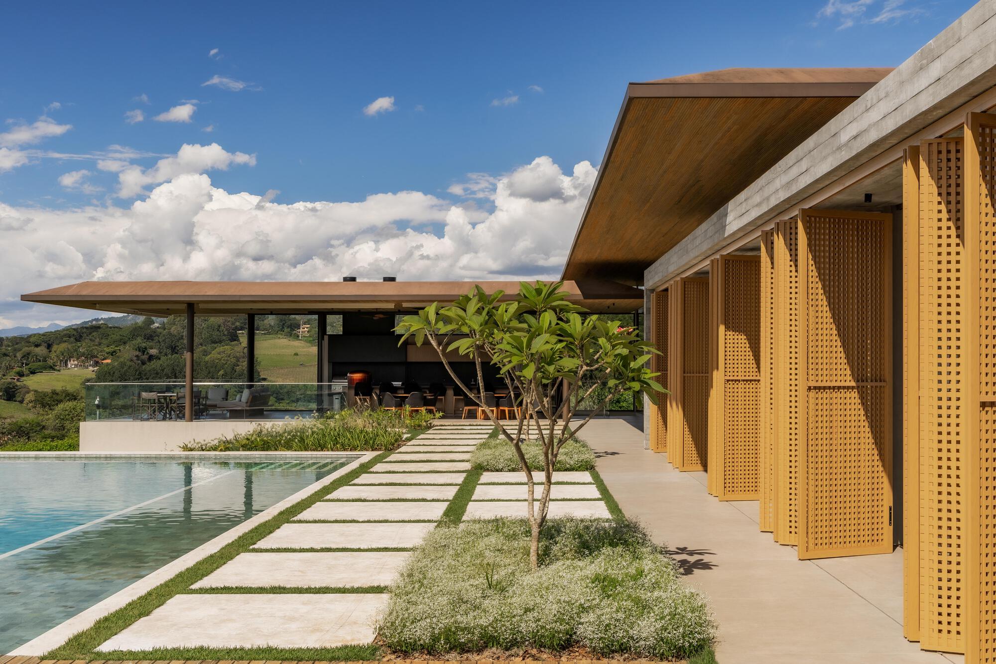 Perforated timber screens beside a reflecting pool with stone pavers and young trees