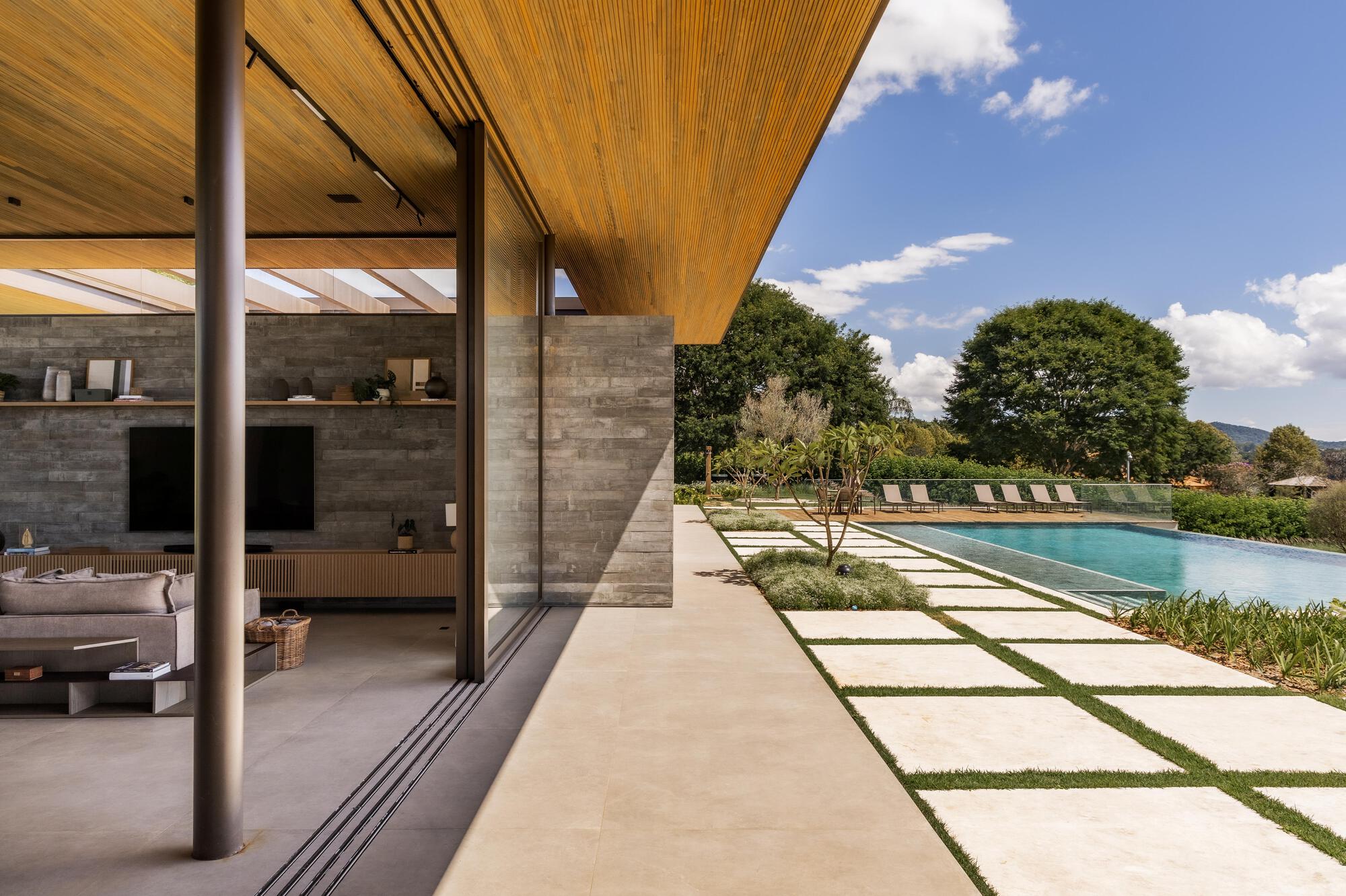 Covered terrace with wood soffit and circular steel columns framing the pool and paving beyond