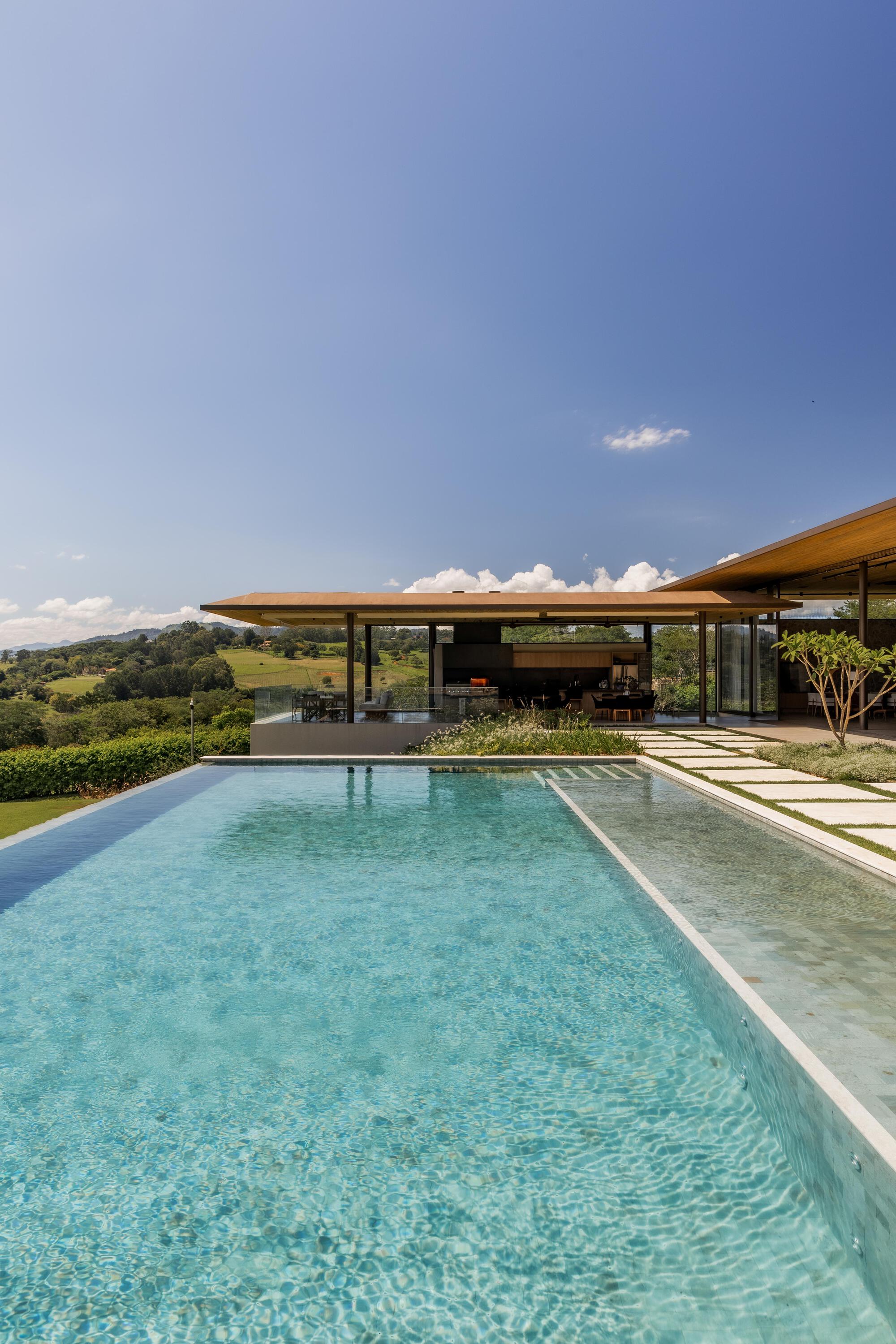 Infinity pool with pale limestone coping and grass-jointed pavers under a clear afternoon sky