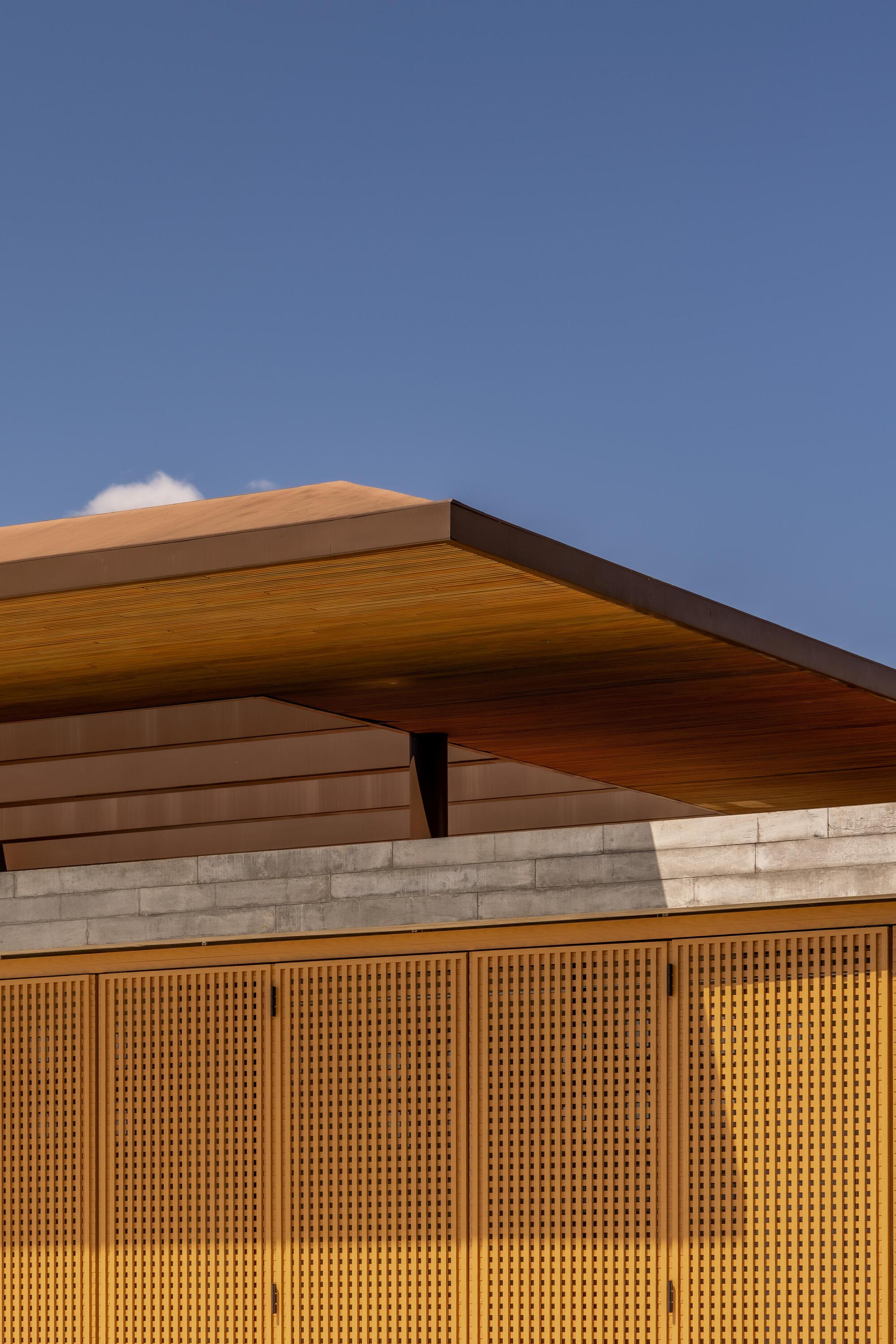 Detail of the angled timber roof eave and perforated wood screen facade at dusk